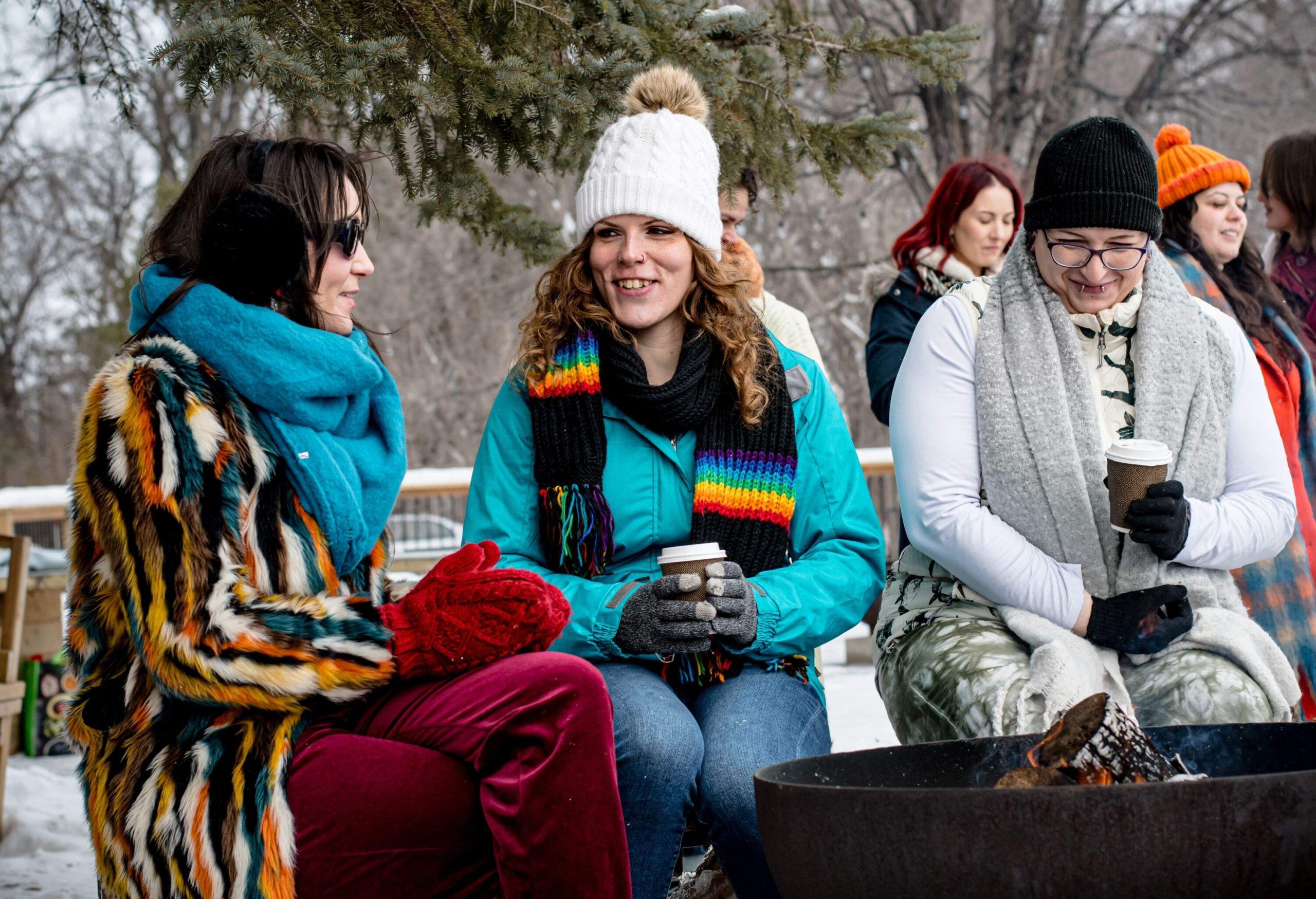 Amidst the winter chill, trans women and their nonbinary neurodivergent friend gather by the fireside, each holding a cup of cocoaâa chosen family of unity and shared warmth in the season's embrace.