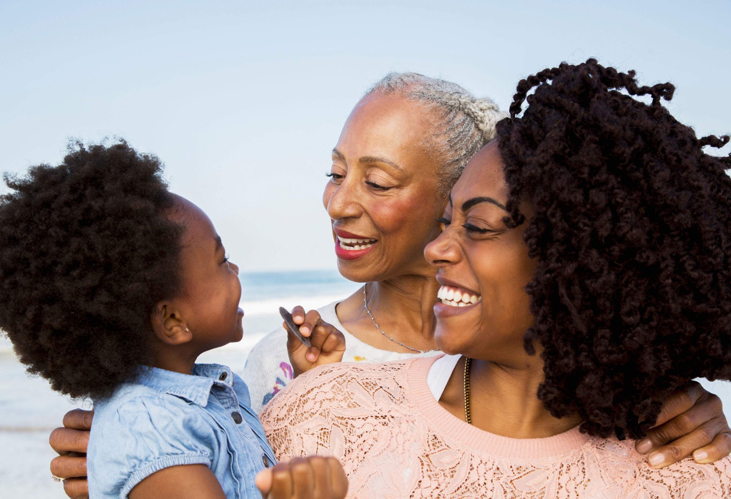 A joyful three-generational family with Afro-styled hair shares smiles and loving glances, cherishing their time together.