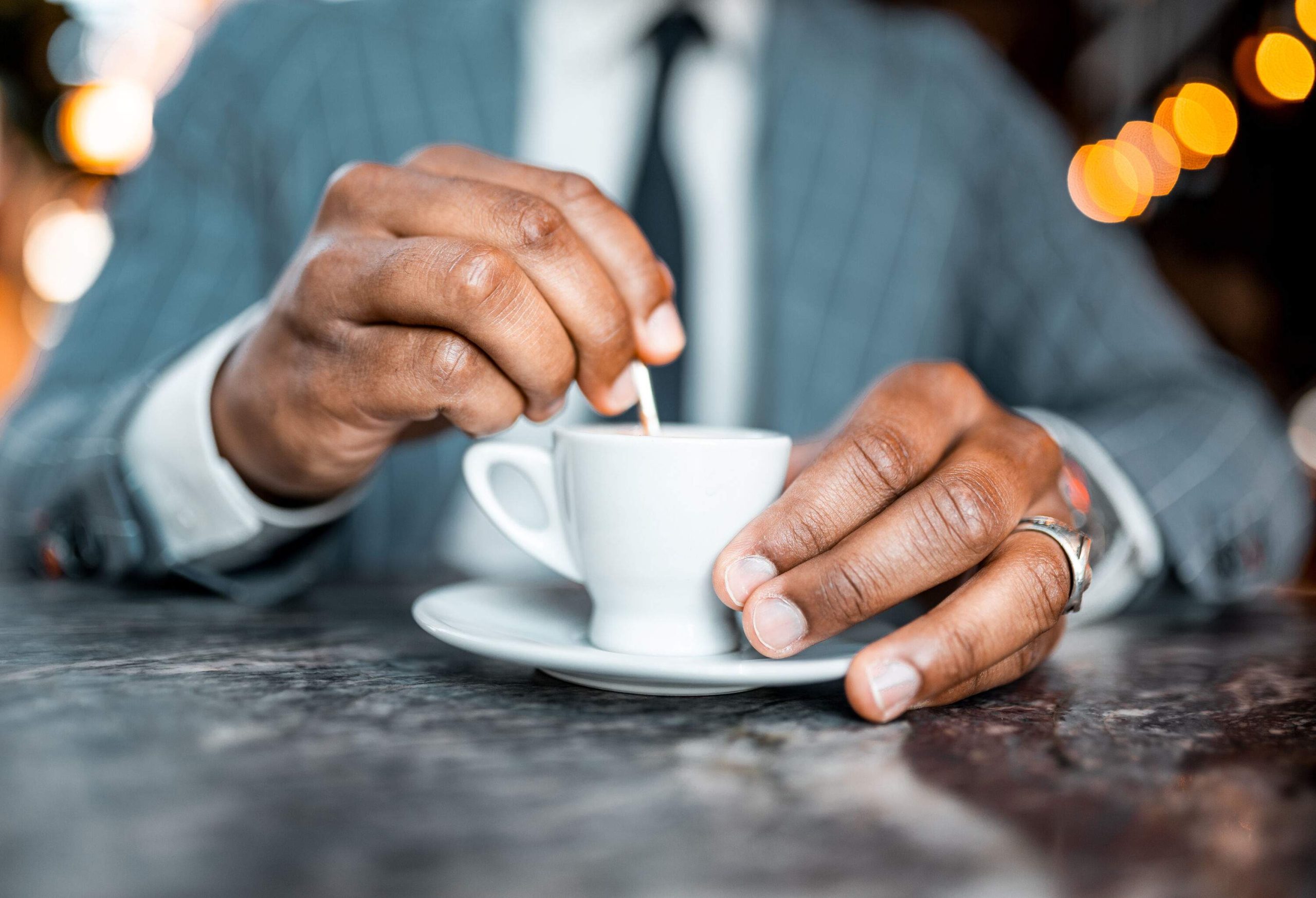 A man in business attire with a small cup of coffee on a table. 