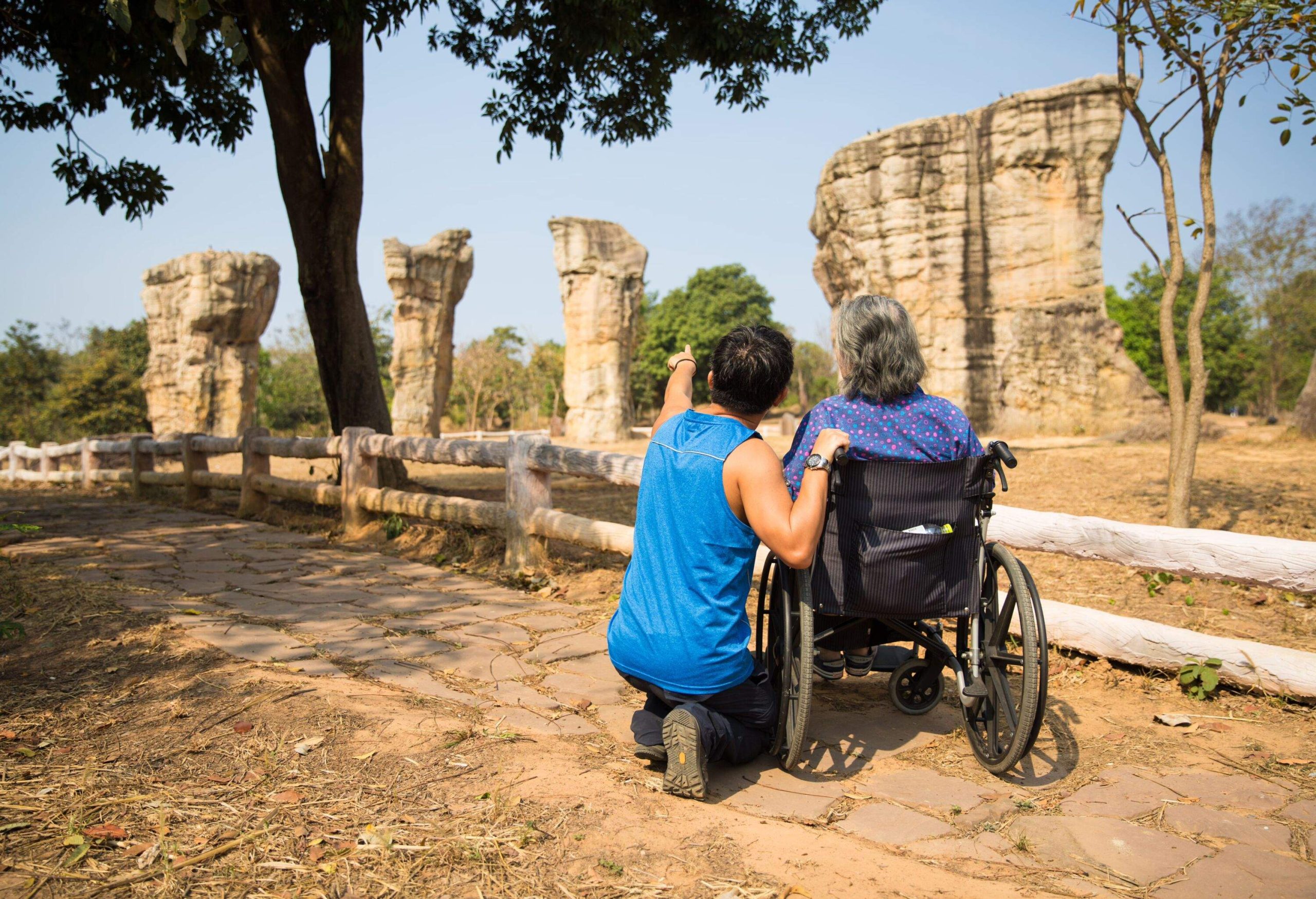 A man wearing blue singlet and black sport pants takes his old mother on wheelchair to see the strange rock formation of Mo Hin Khao (Thailand's Stonehenge) in Chaiyaphum Province, Thailand.