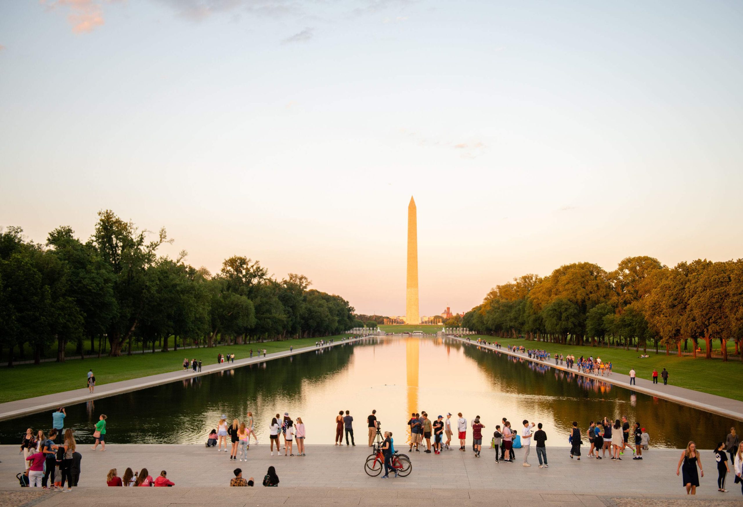 A crowded staircase in front of a pond with an obelisk in the distance.