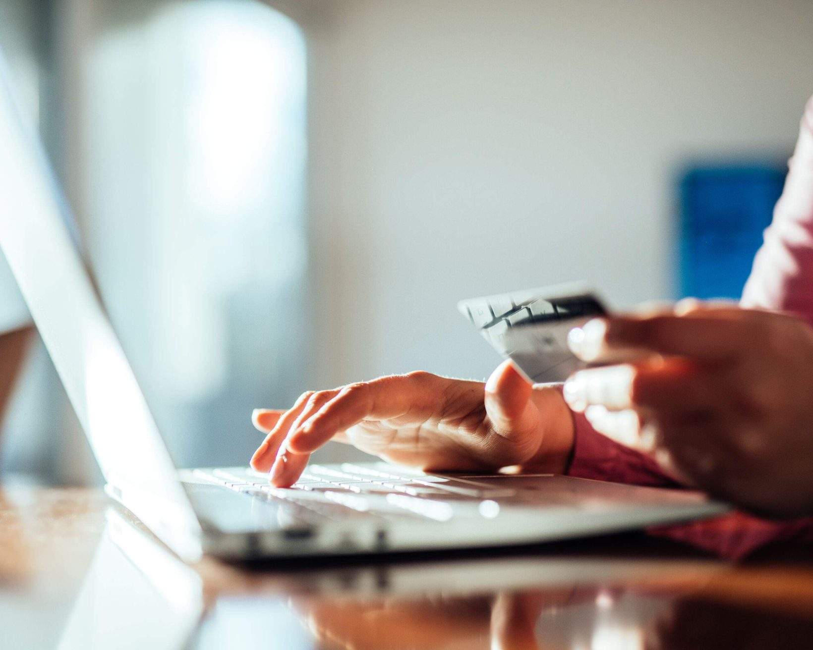 The right hand types on a laptop while the left hand holds a credit card.