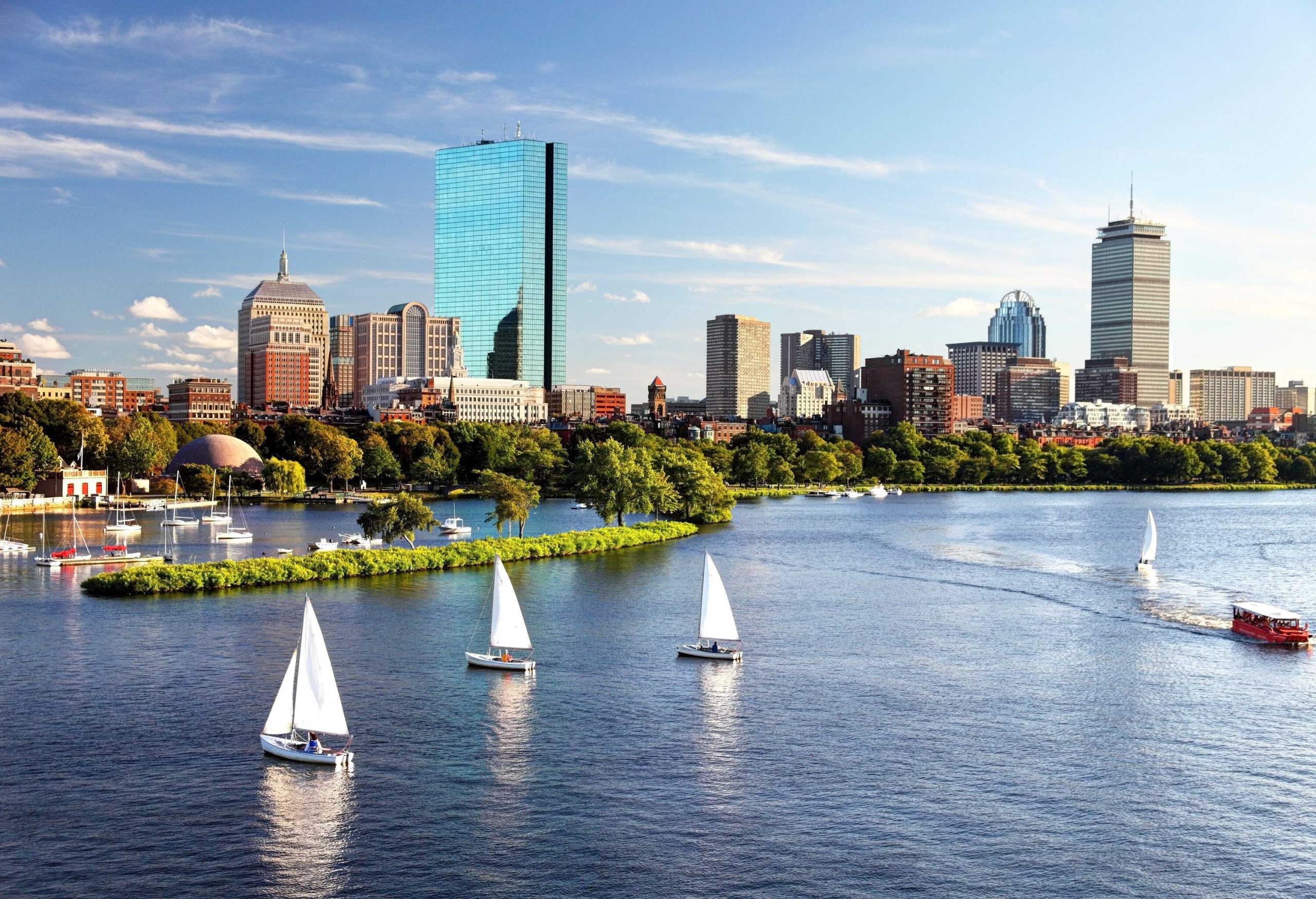 White sailboats on a river overlooking the modern city skyline with towering skyscrapers.