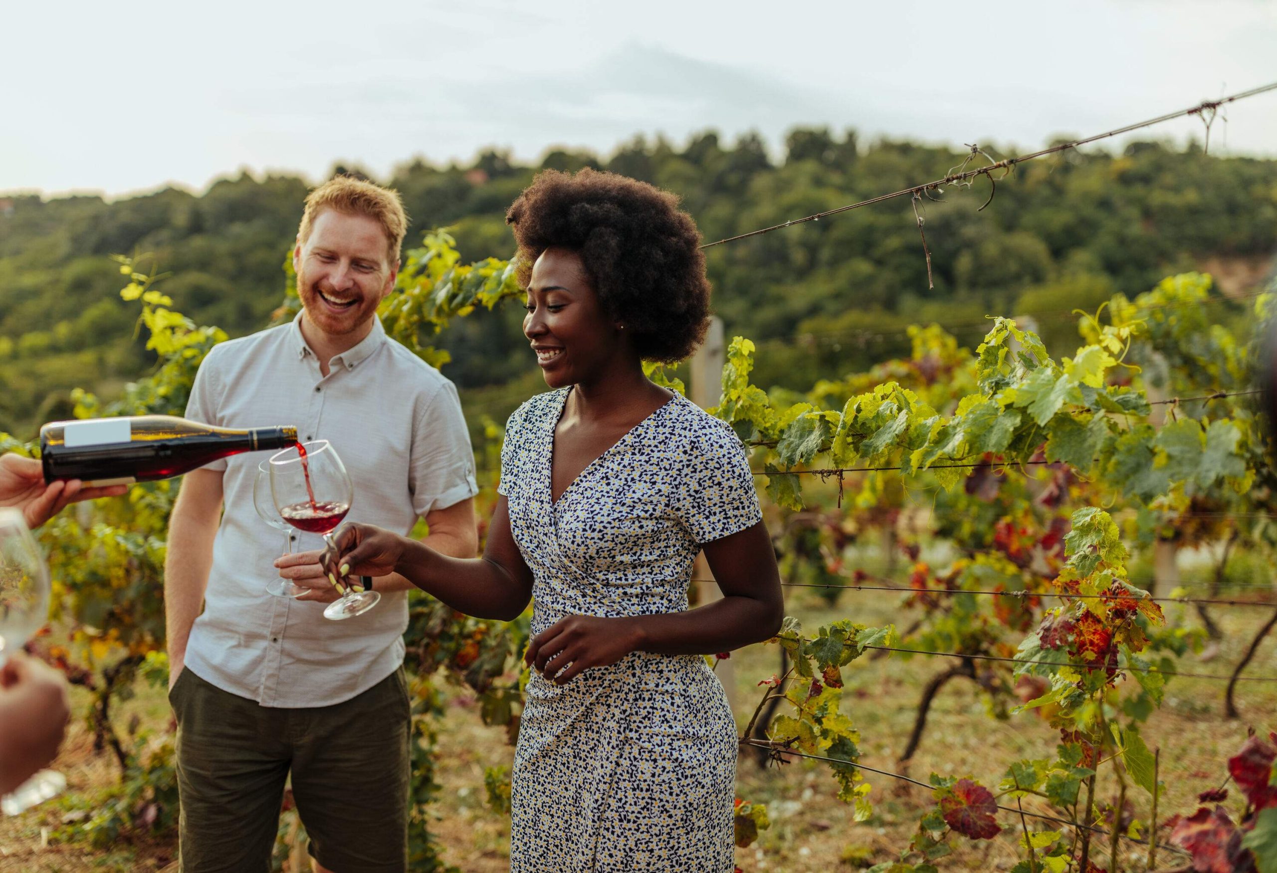 A woman getting her wine glass filled in a vineyard.