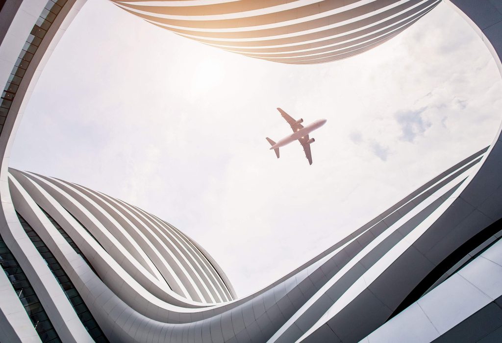 An airplane in flight framed by the continuous curve of a building.