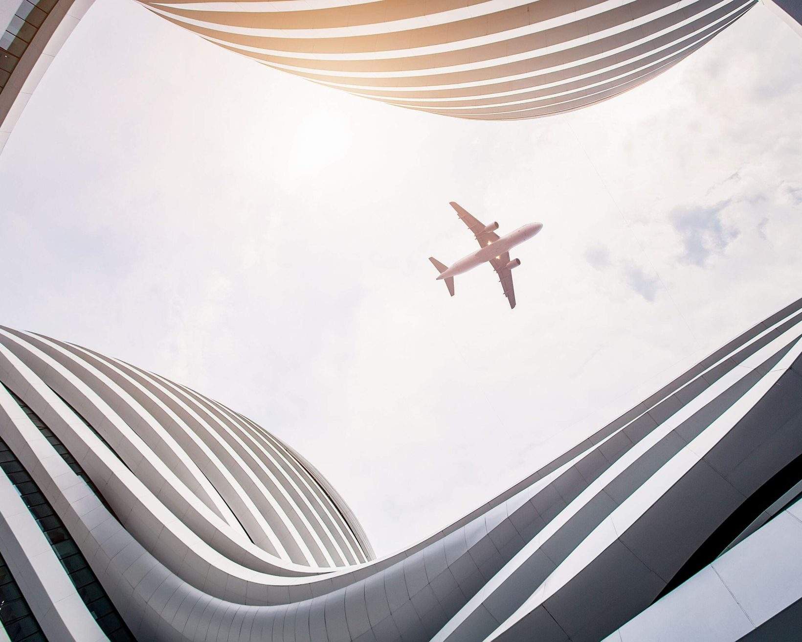 An airplane in flight framed by the continuous curve of a building.