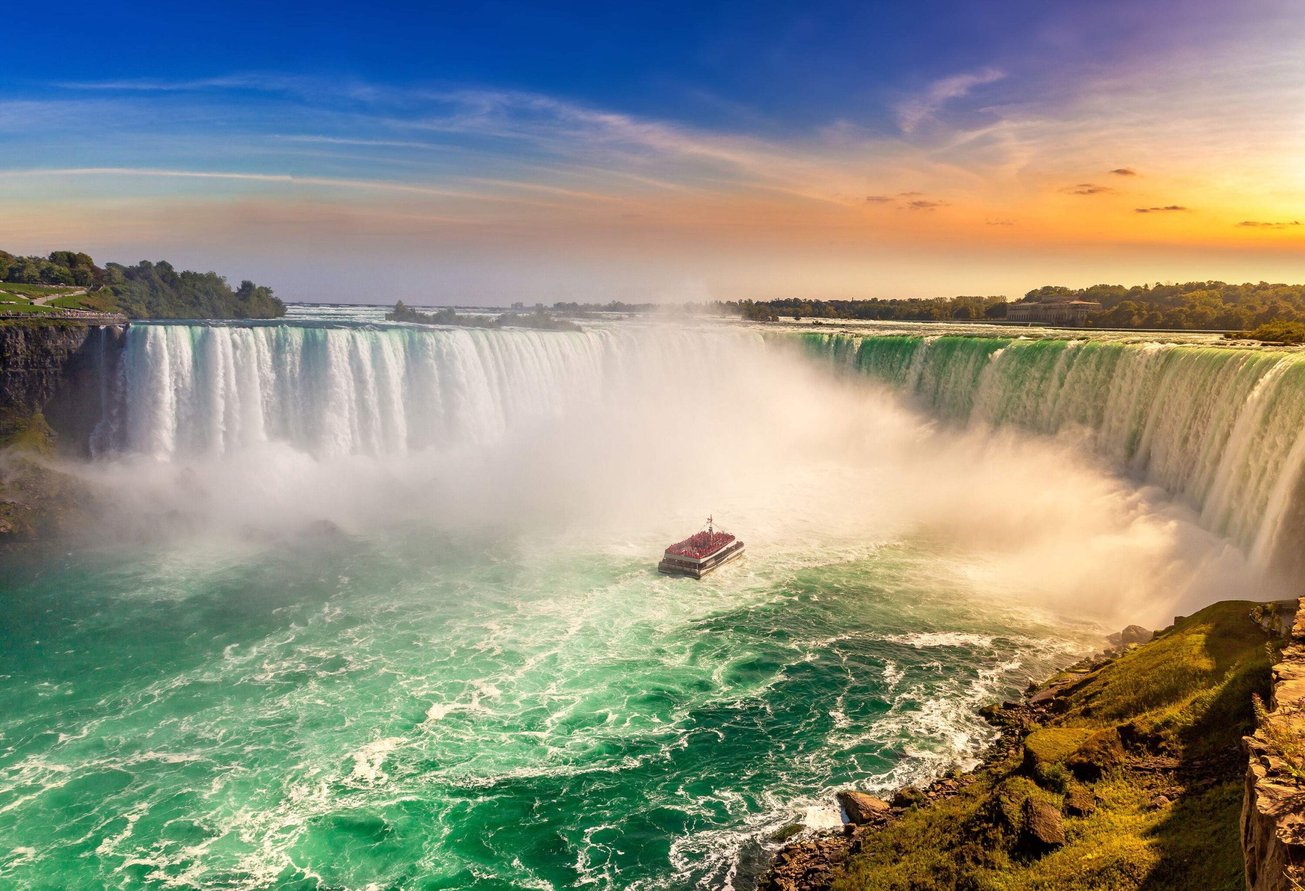 A boat approaching the base of a raging and massive waterfall.