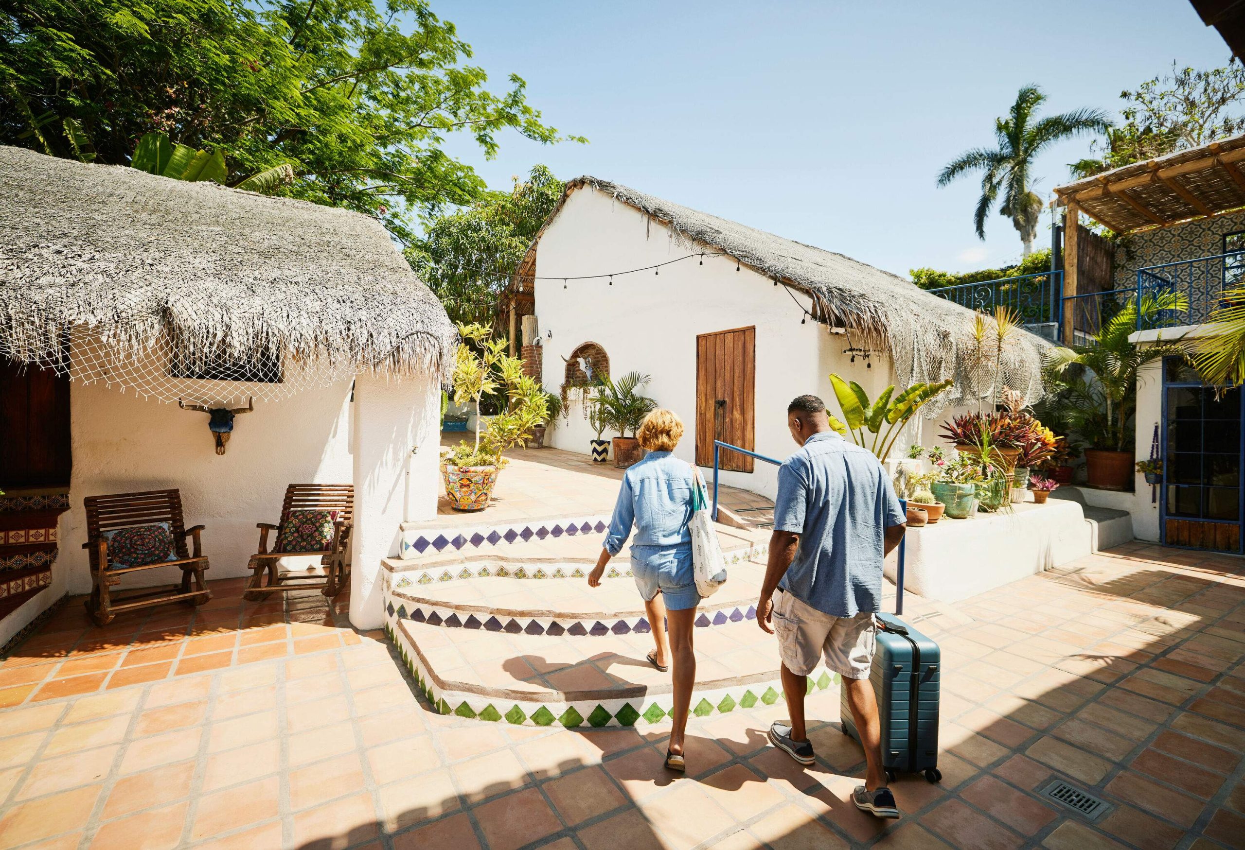 A couple walking across the tiled floor of a resort with their luggage in tow.