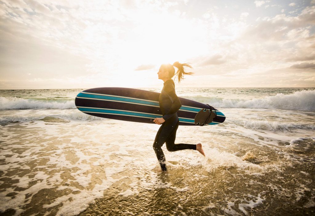 A female surfer sprinting into the ocean, her surfboard on her side.