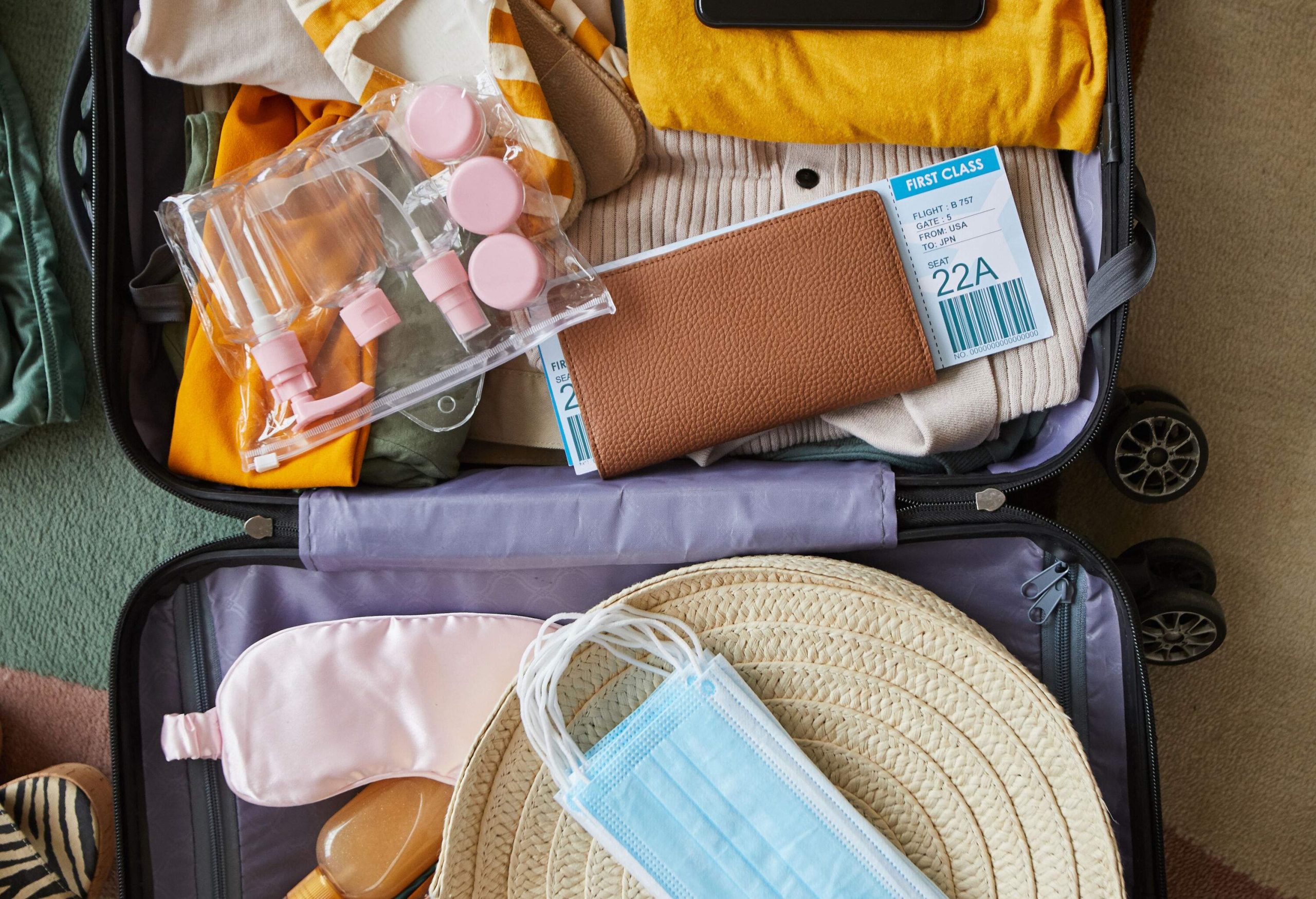 Luggage with colourful travelling essentials with facemasks, refillable bottles and a passport.