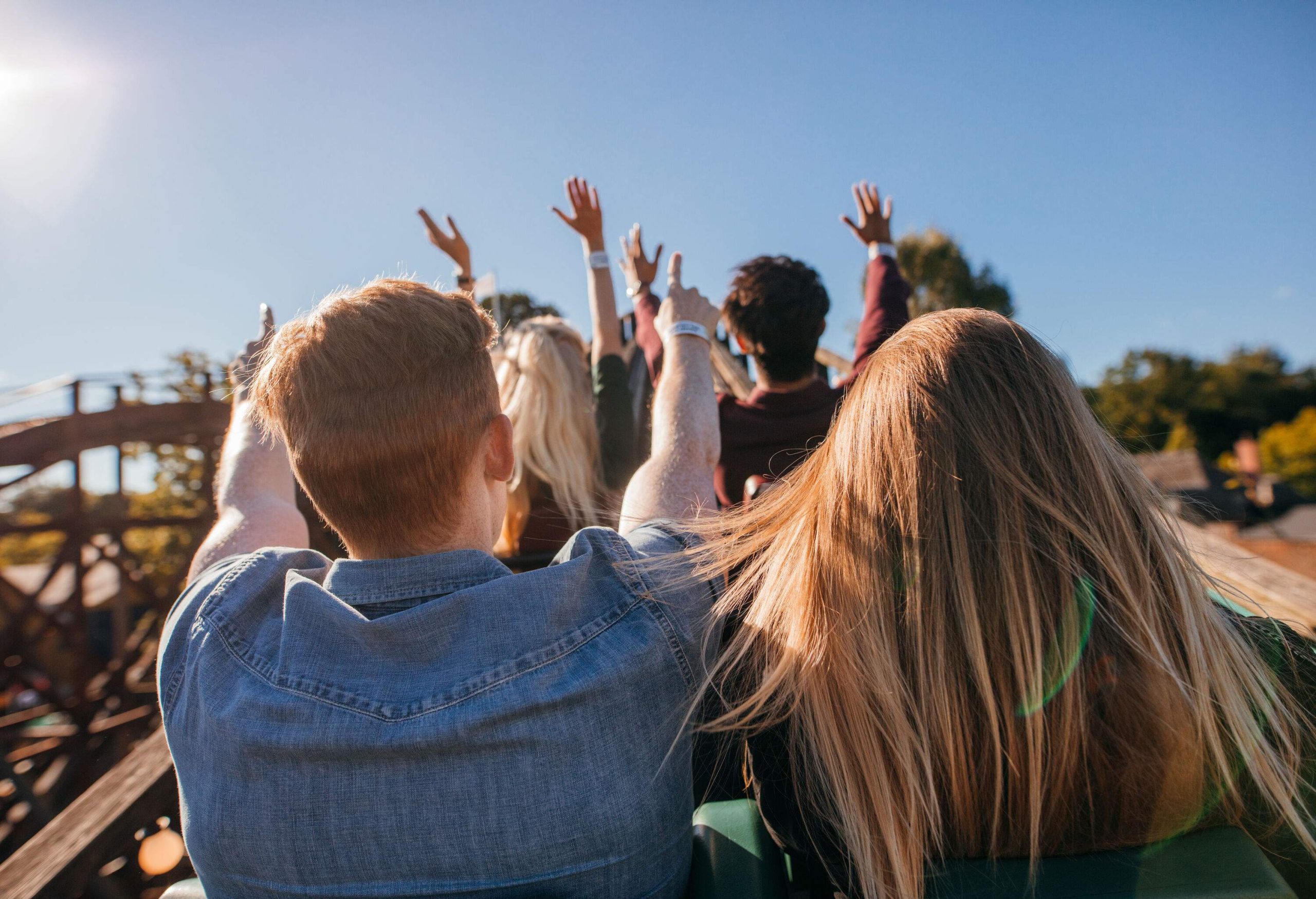 People on a roller coaster ride raise their hands.