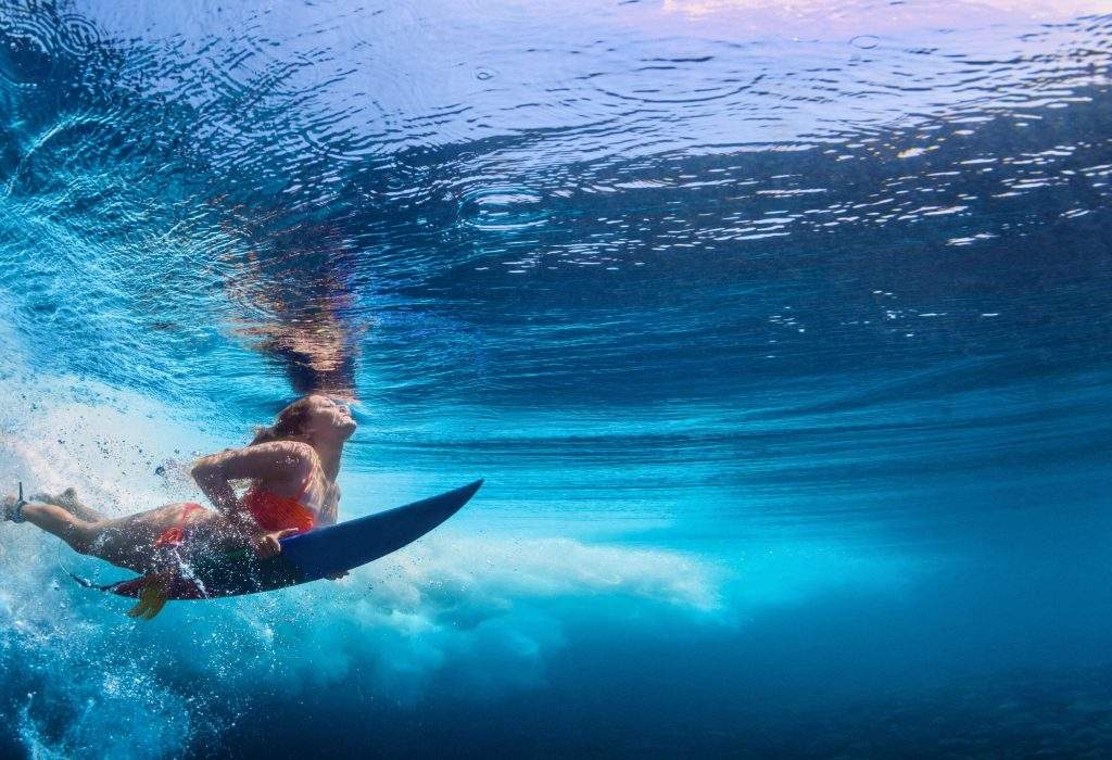 A woman in an orange bikini is submerged in sea water while surfing.