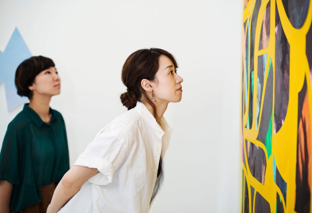 A woman in a white shirt looks intently at an abstract art on the wall.