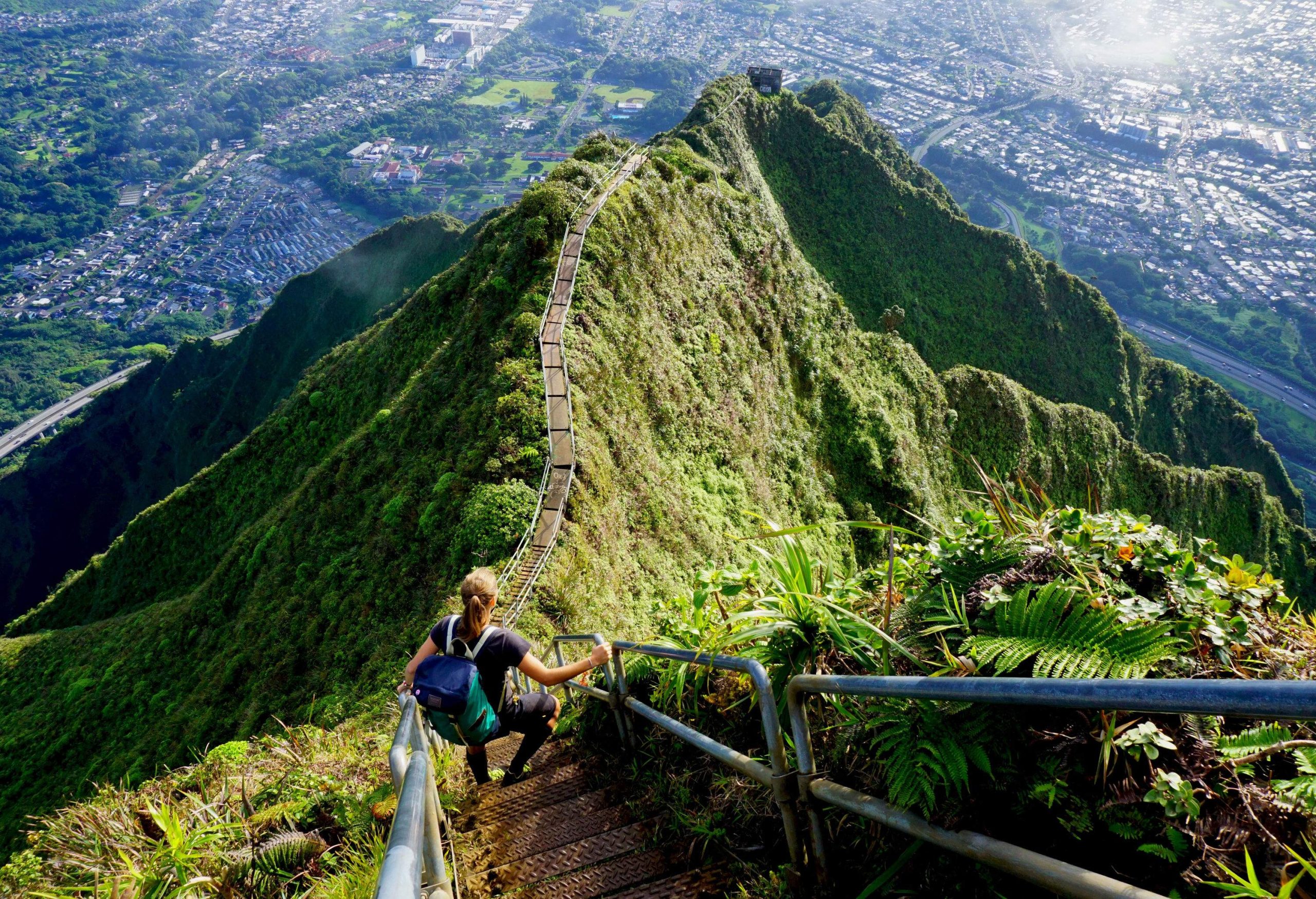 An adventurous individual carefully descends the famed Haiku Stairs, a series of steep and narrow steps carved into the lush mountaintop and surrounded by vibrant green vegetation and stunning panoramic views, navigating the challenging ascent with focus and determination.