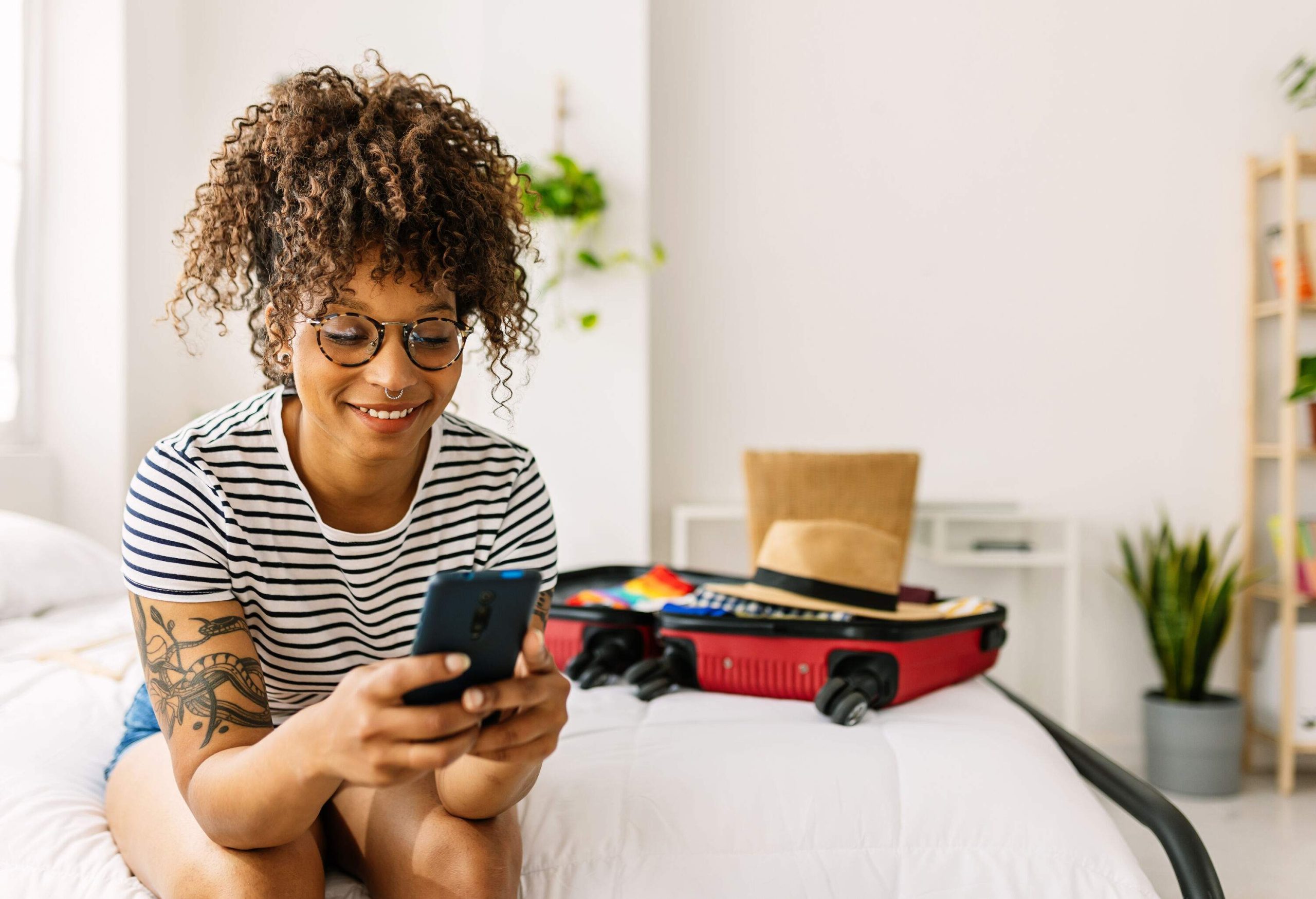 Happy young woman booking a hotel room while packing her summer suitcase for holidays