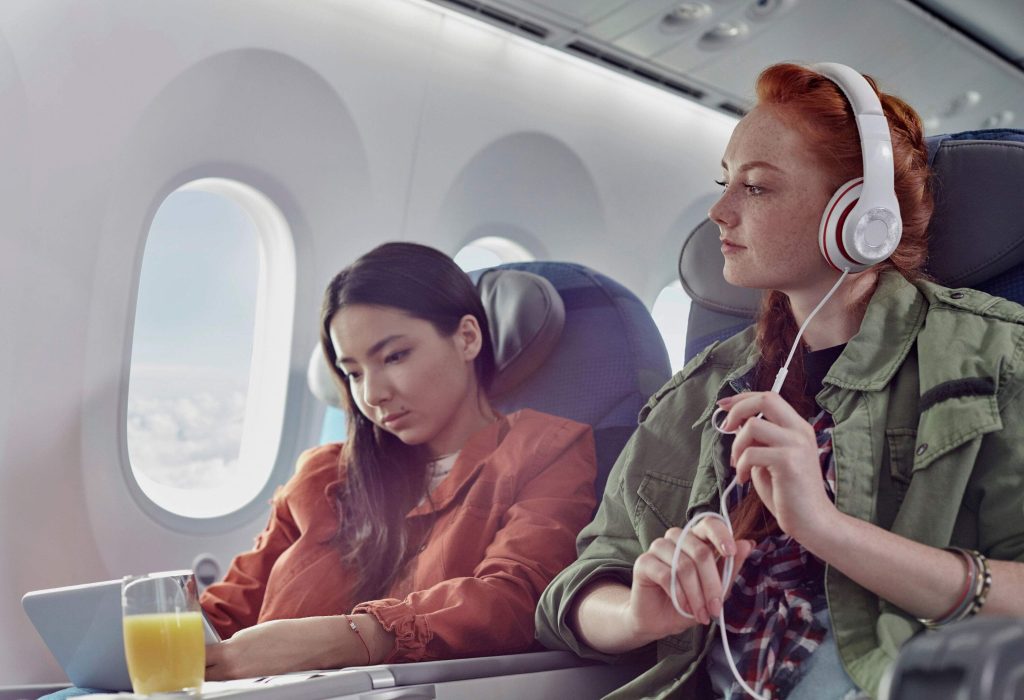 Two female passengers on a flight, one watching something on her laptop and the other listening to music through headphones.