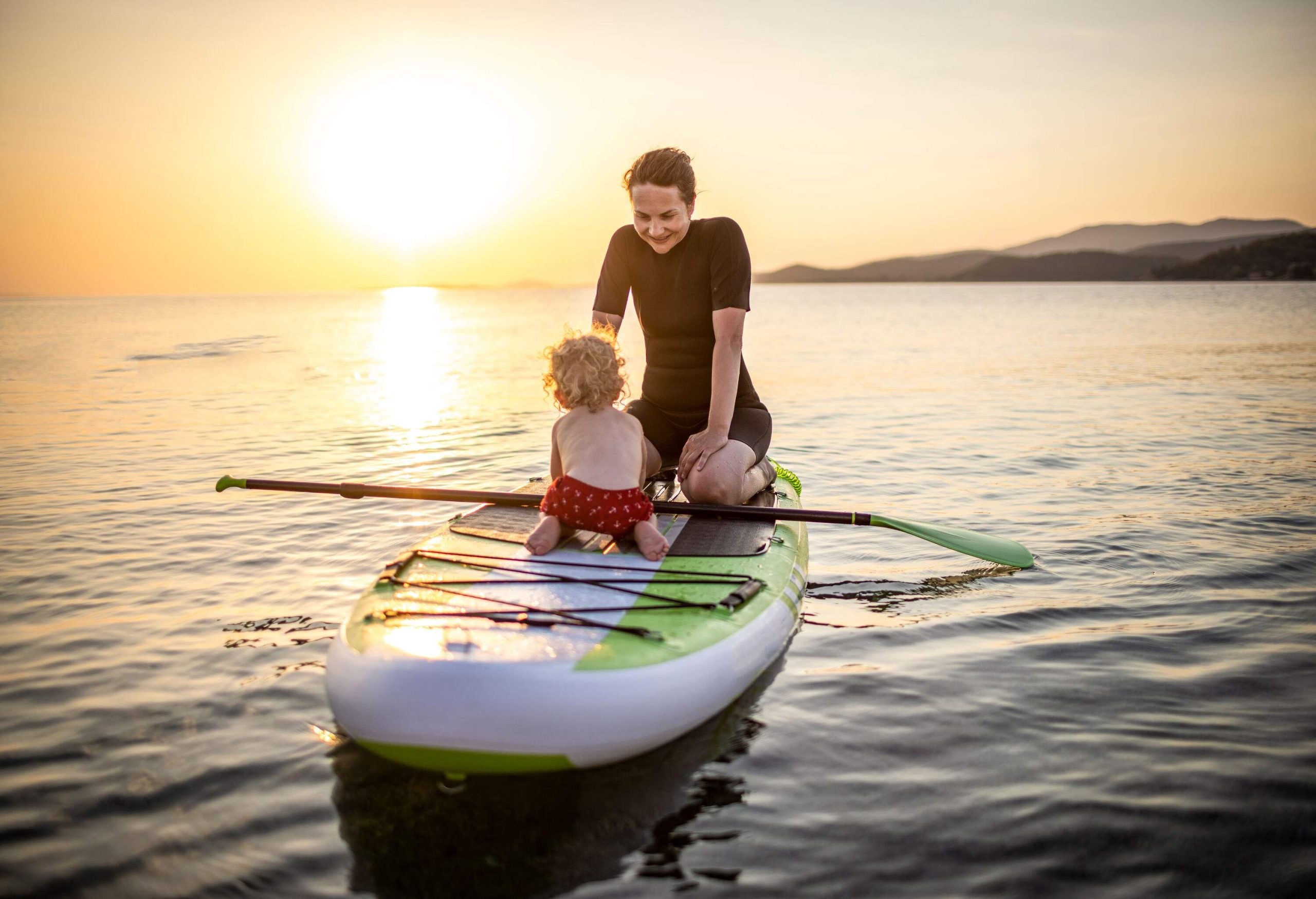 A woman and a little boy riding a paddleboard in the sea.