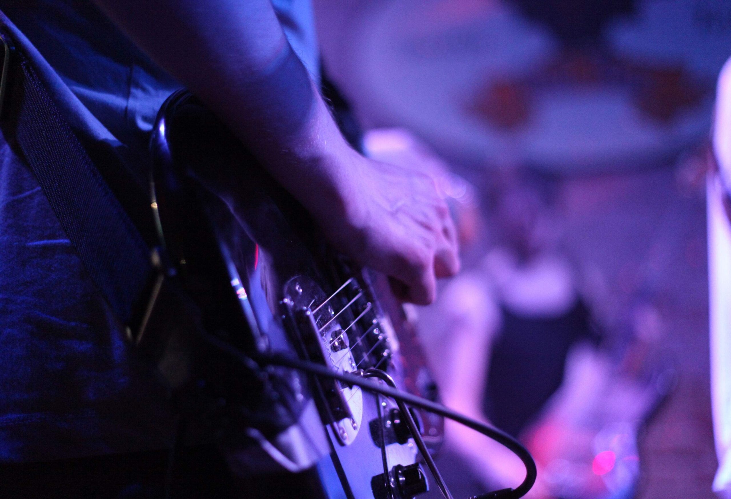 A hand strums an electric guitar under blue lights.