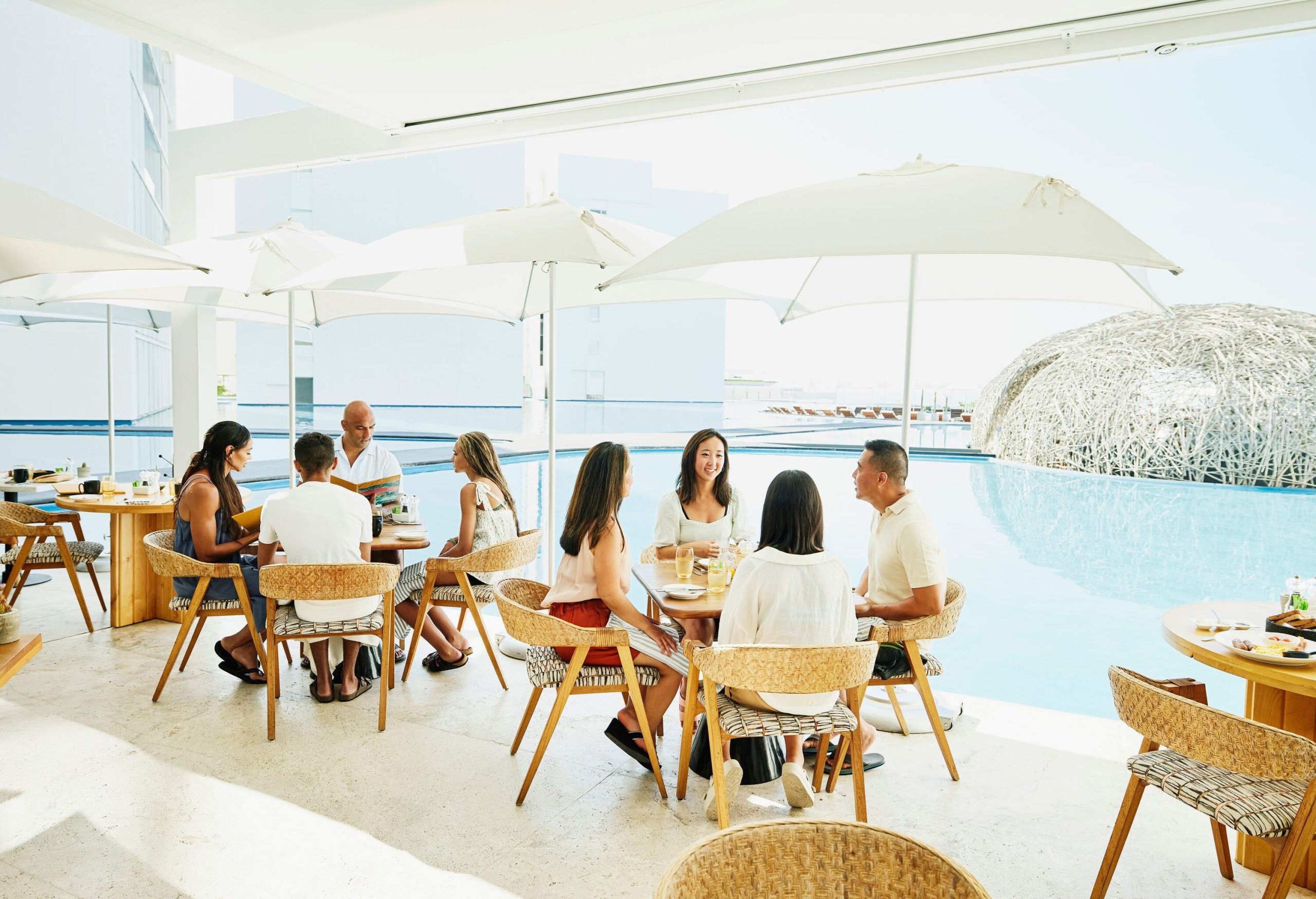 Wide shot of smiling families seated for breakfast at outdoor restaurant at luxury tropical resort while on vacation