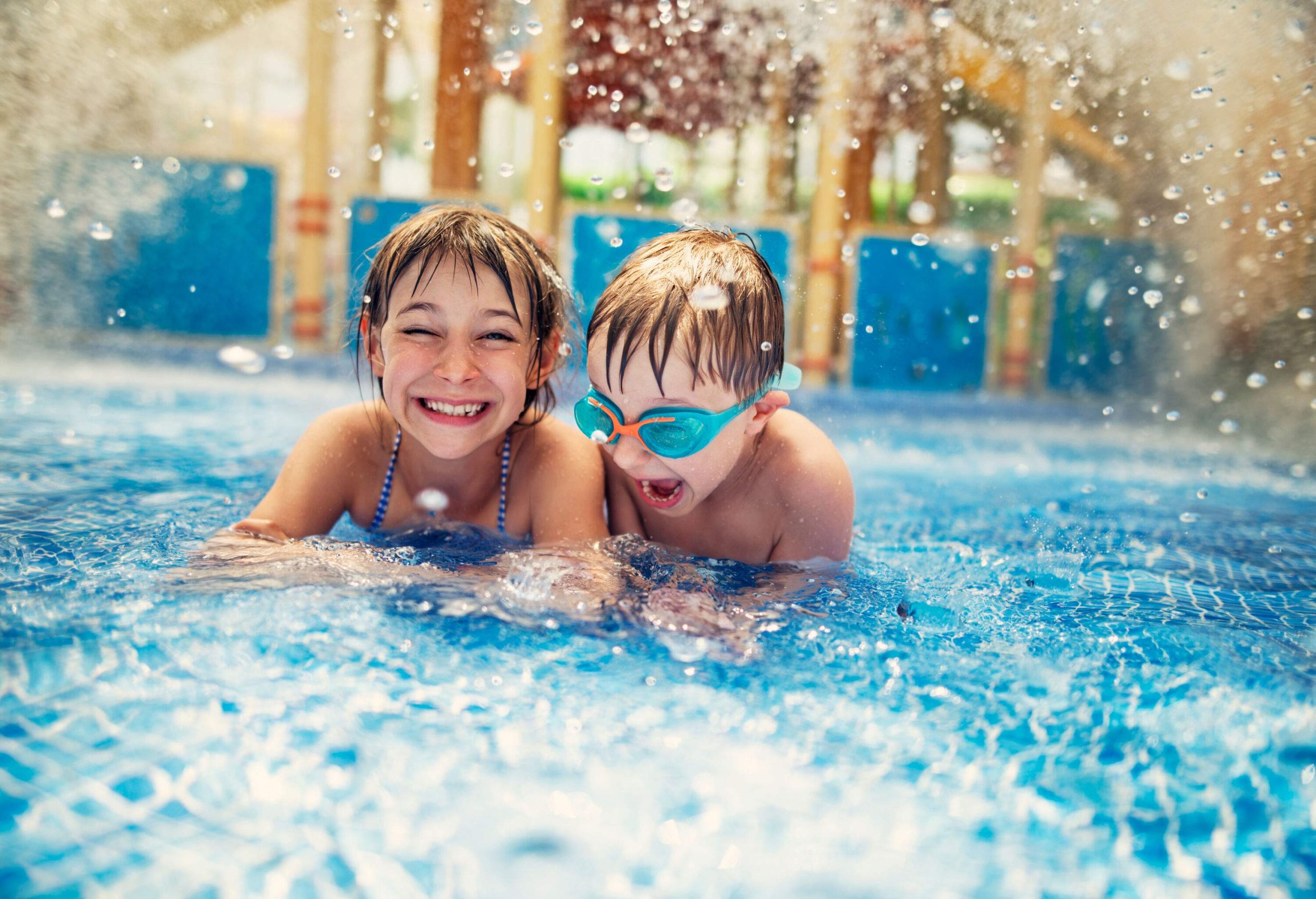 Water splashing over two children playing in a swimming pool.