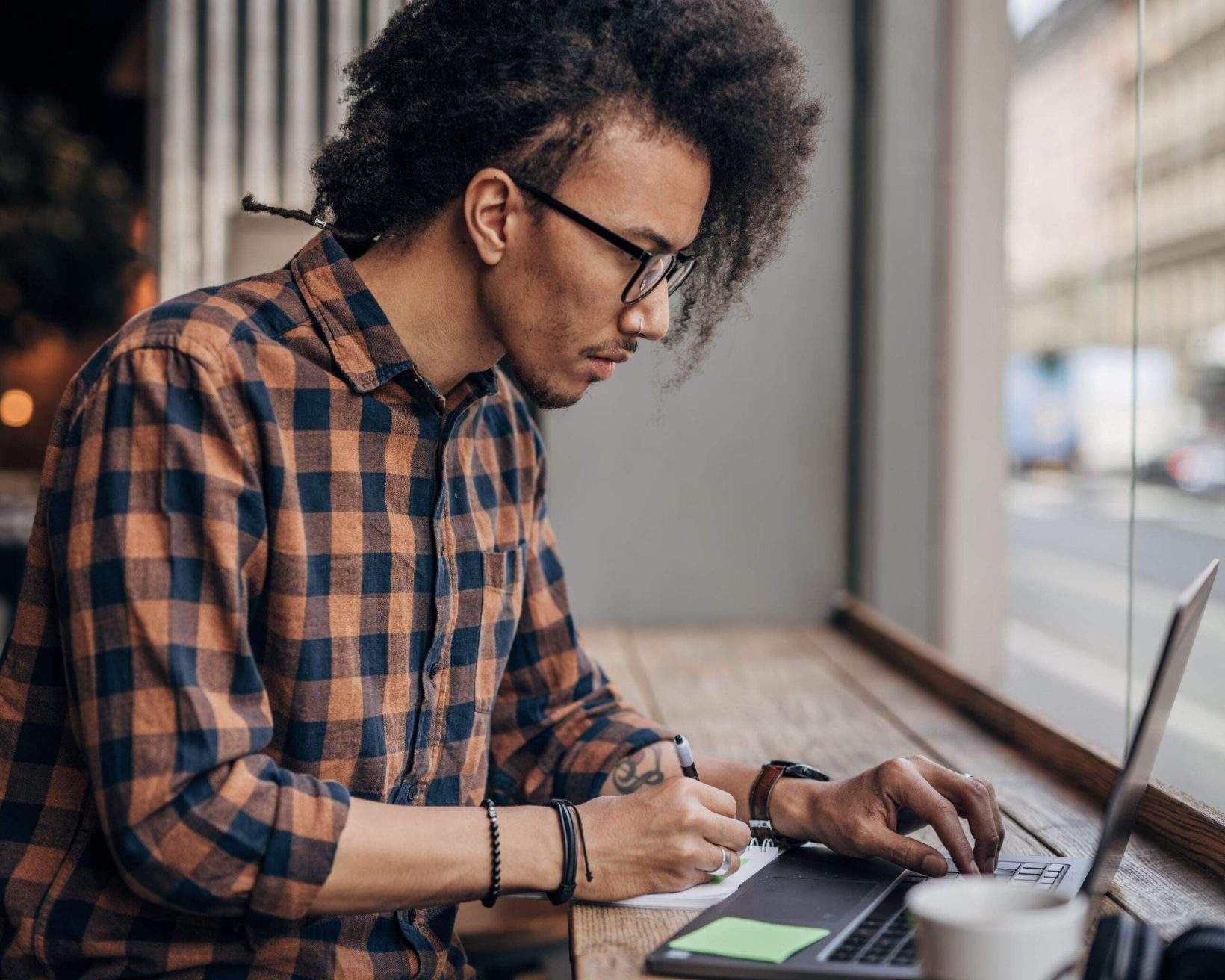 Young man using laptop in coffee shop writing something