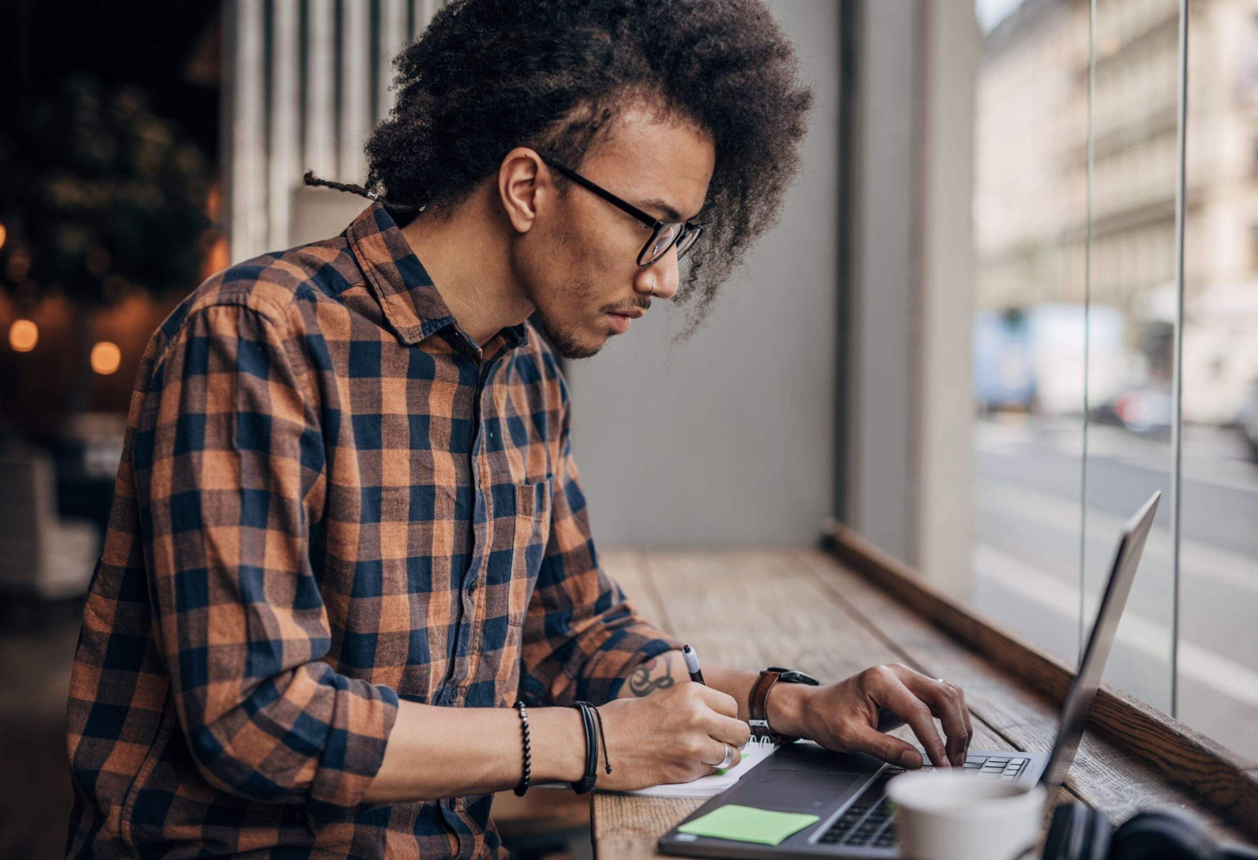 Young man using laptop in coffee shop writing something