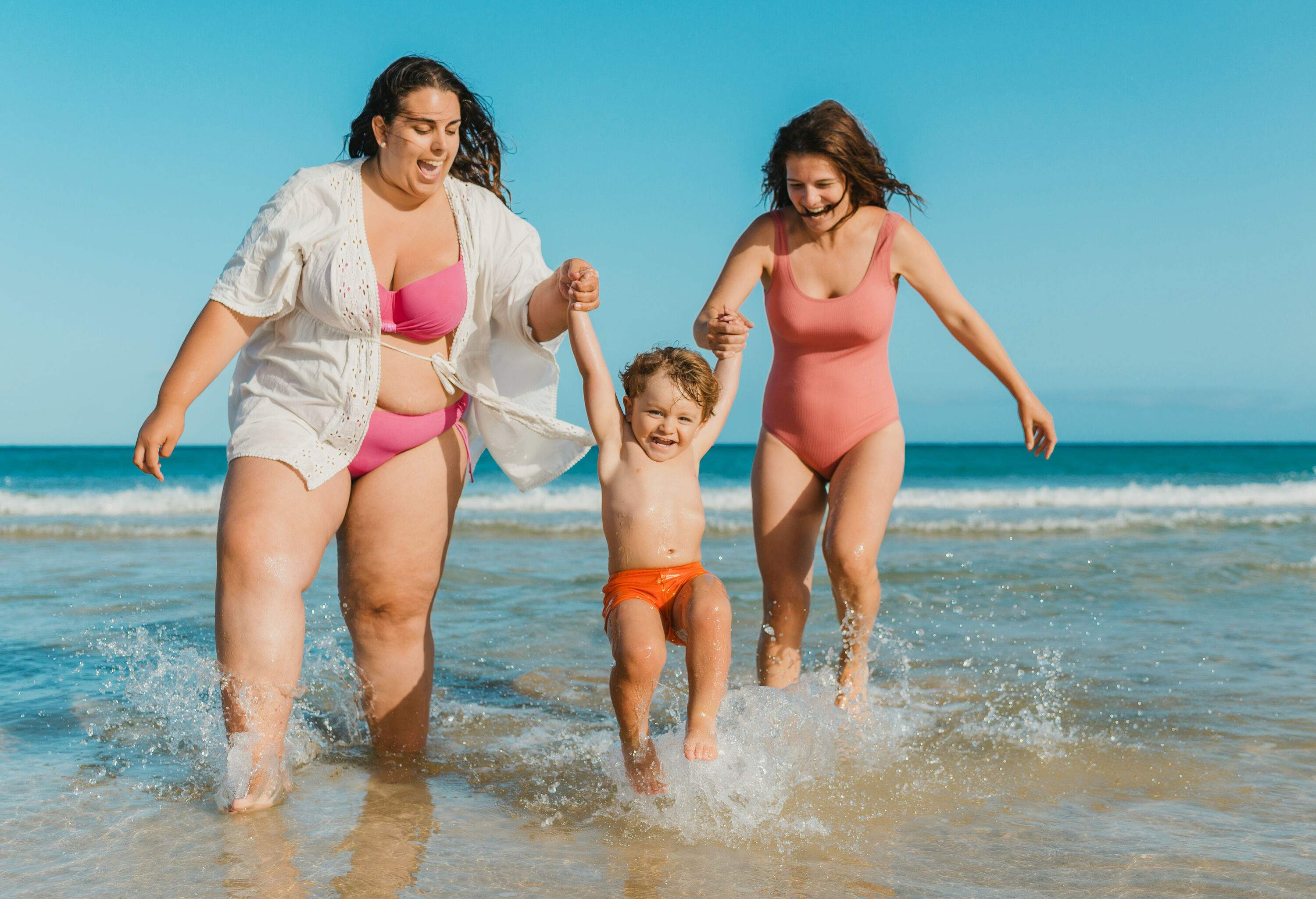 A little boy laughing as he is being lifted out of the water by two women.