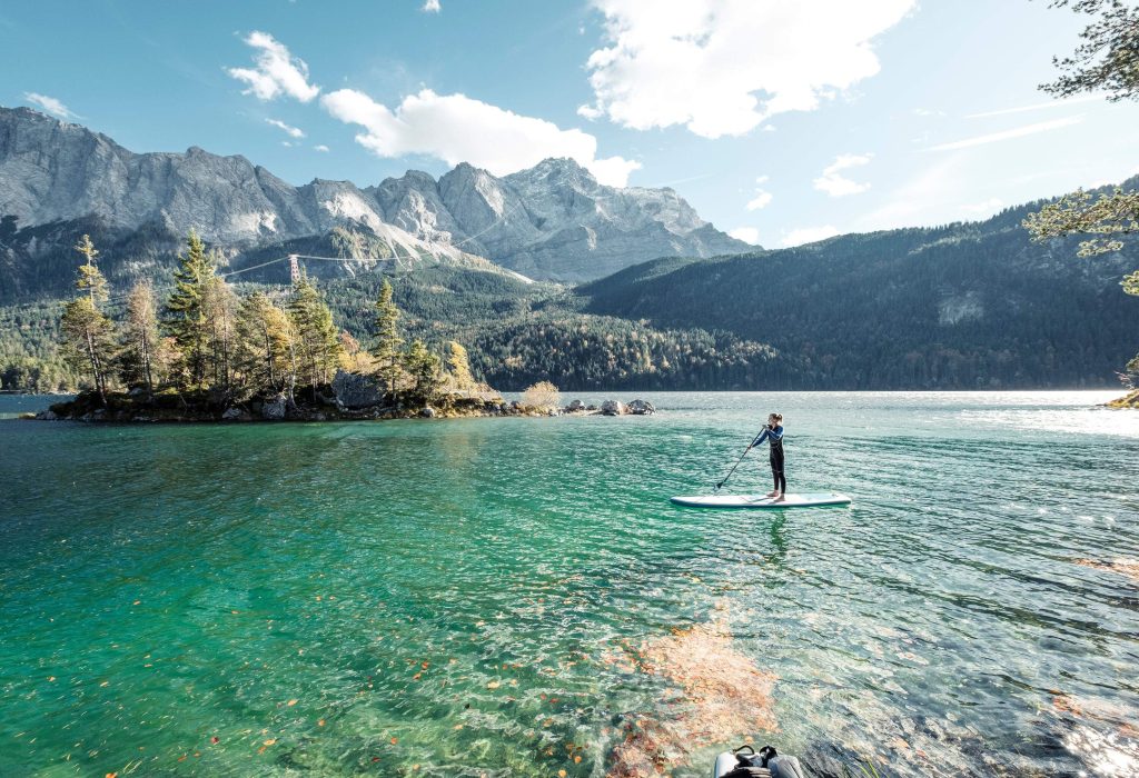 A female standup paddleboarder floating on a serene lake surrounded by craggy mountains.