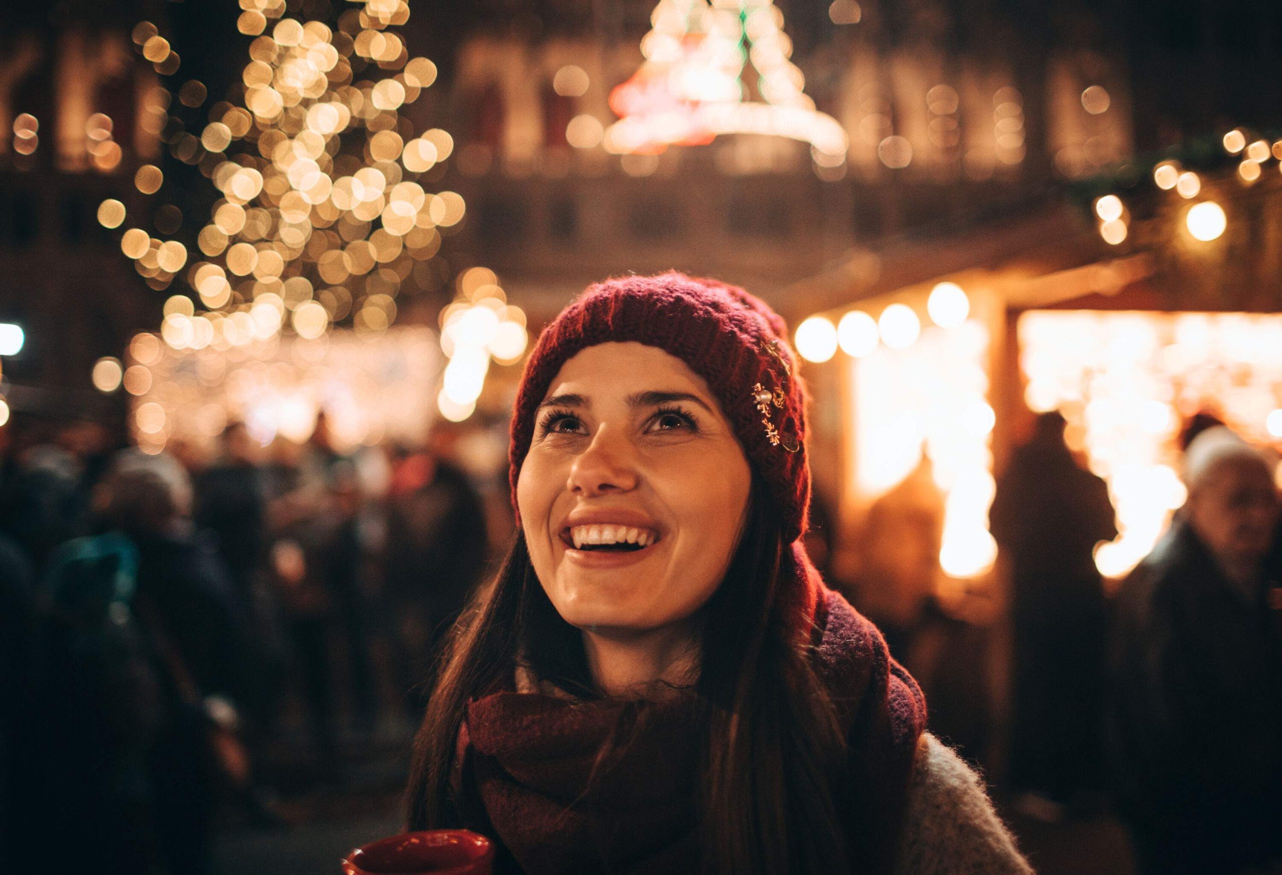 A cheerful young woman with flashing lights behind her holding a red mug.