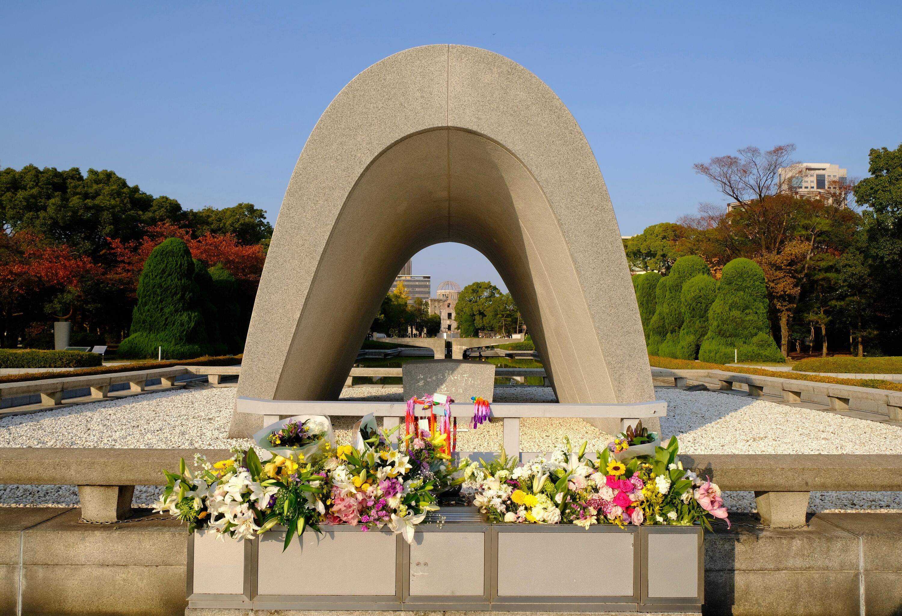 The Hiroshima Victims Memorial Cenotaph is a long, curved concrete structure that resembles an ancient tomb open at both ends.