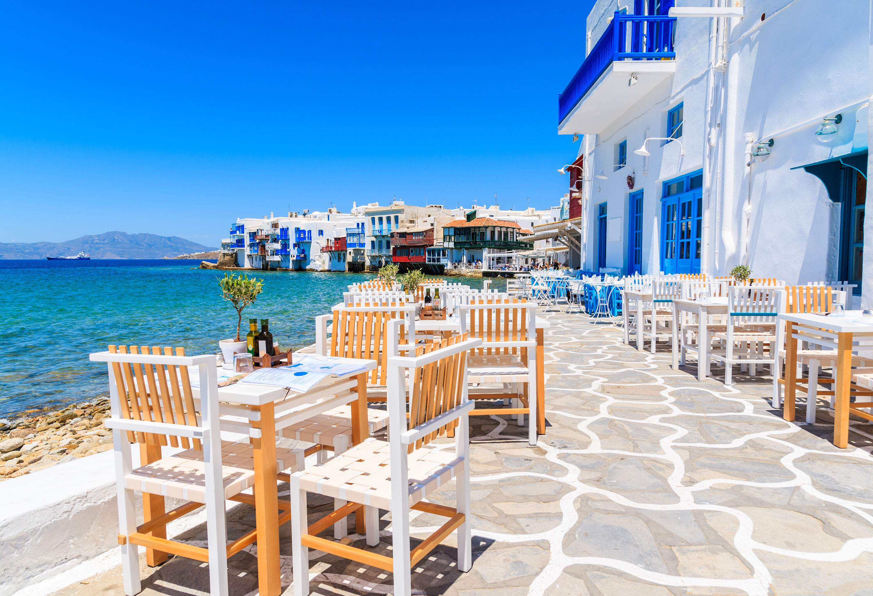 A typical cobbled promenade in Greece with outdoor cafes and whitewashed buildings.
