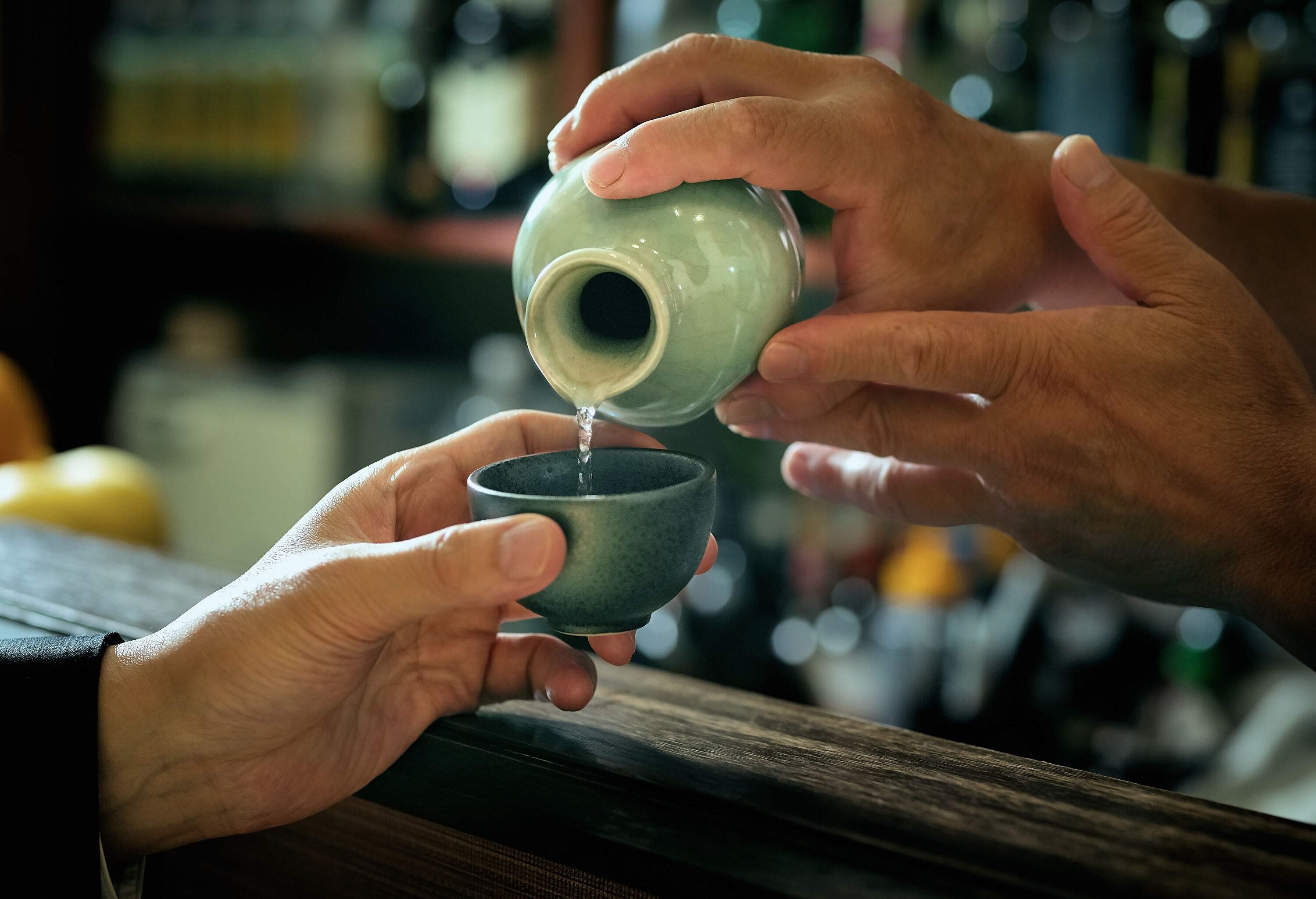 An individual pouring clear liquor into the traditional sake cup.