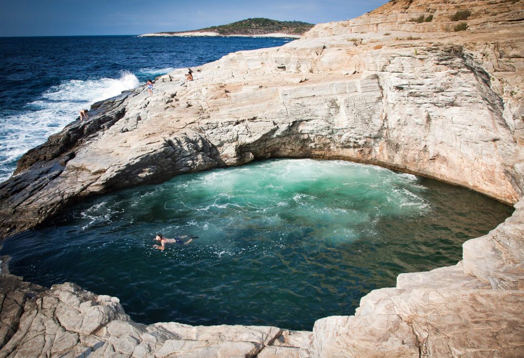 A person swims in a natural rock pool beside an ocean with rough waves.