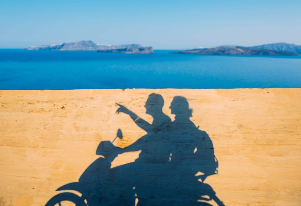 A shadow of two individuals on a motorbike against the blue sea.