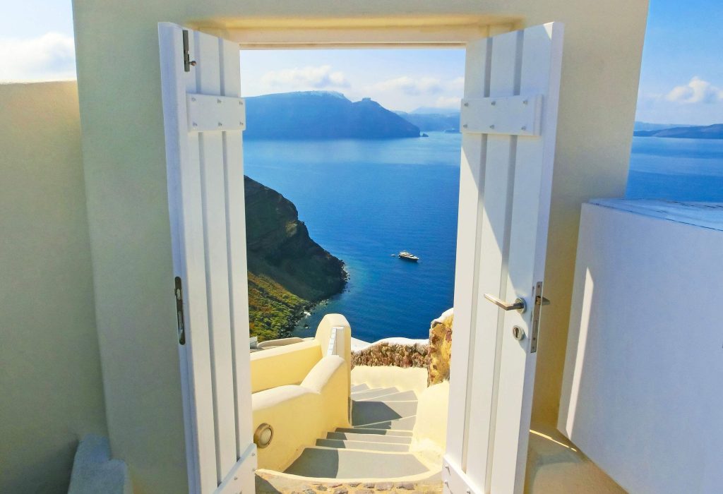 A white opened door that leads to a staircase with overlooking views of a cruising boat in a large ocean.