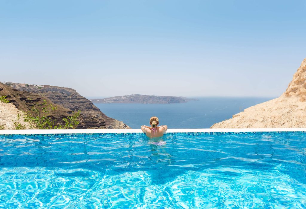 A woman in a swimming pool overlooking the rocky islands and the calm blue sea.