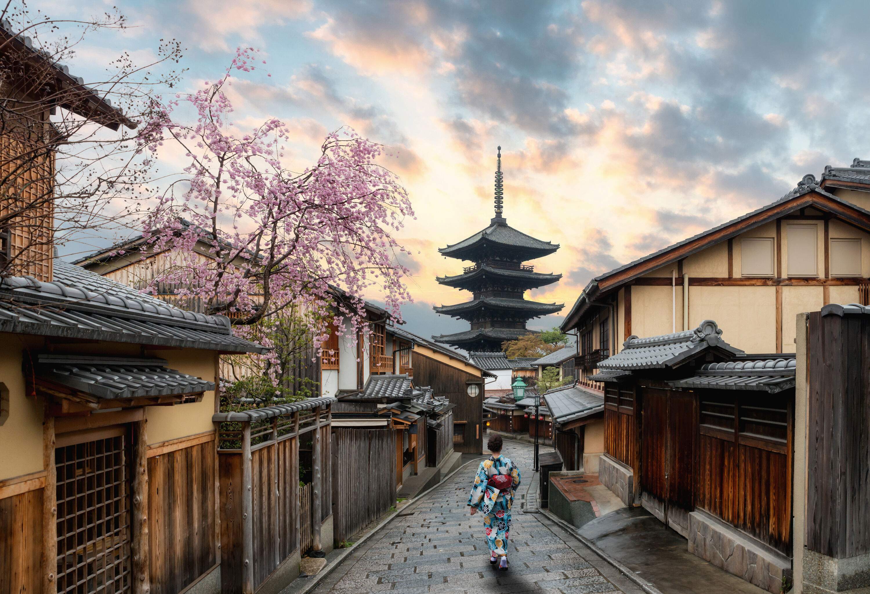 A woman donning a colourful kimono walking down a paved alley with a pagoda in the backdrop.