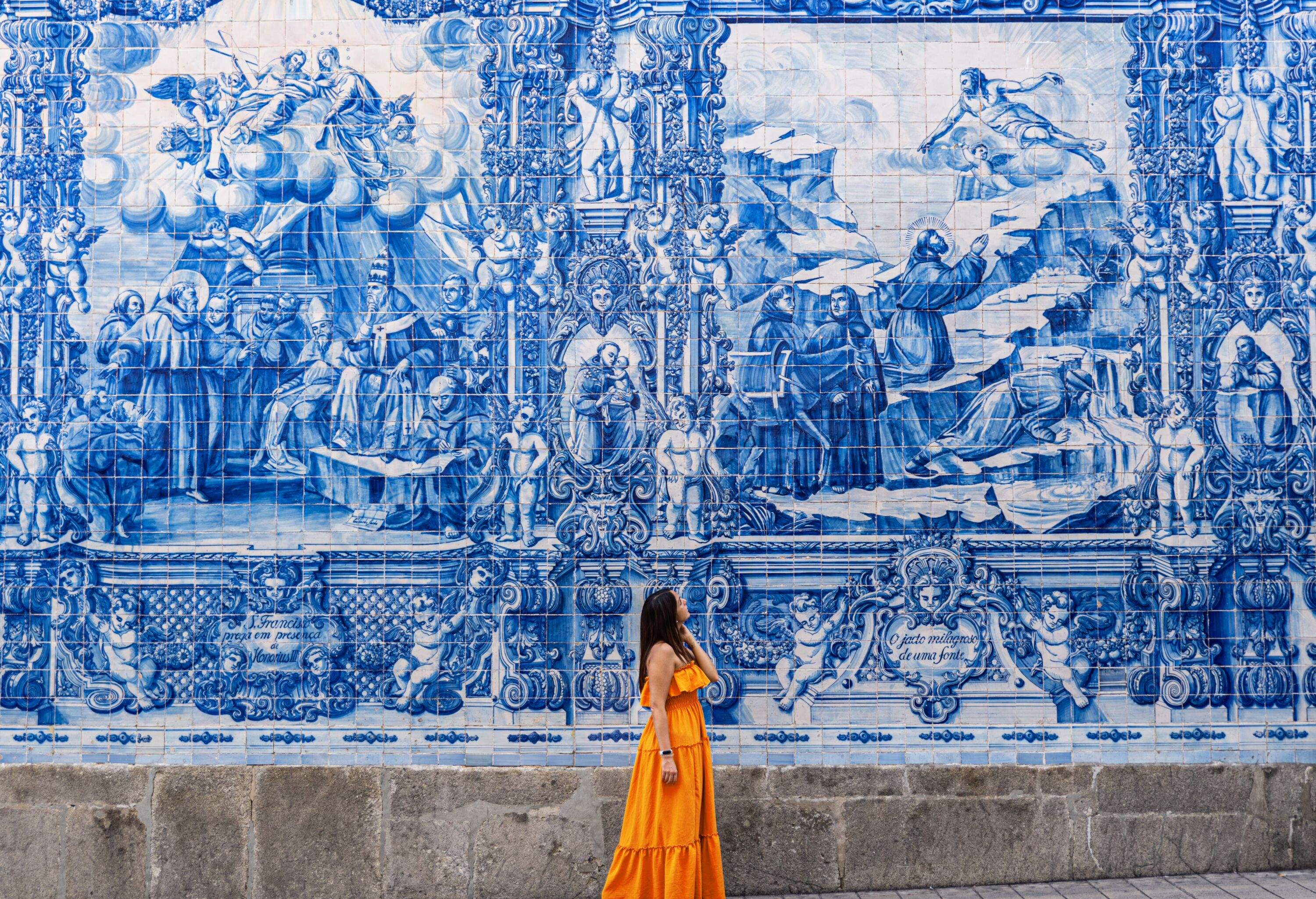 Woman in an orange dress gazing at old decorative traditional azulejo tiles in a city