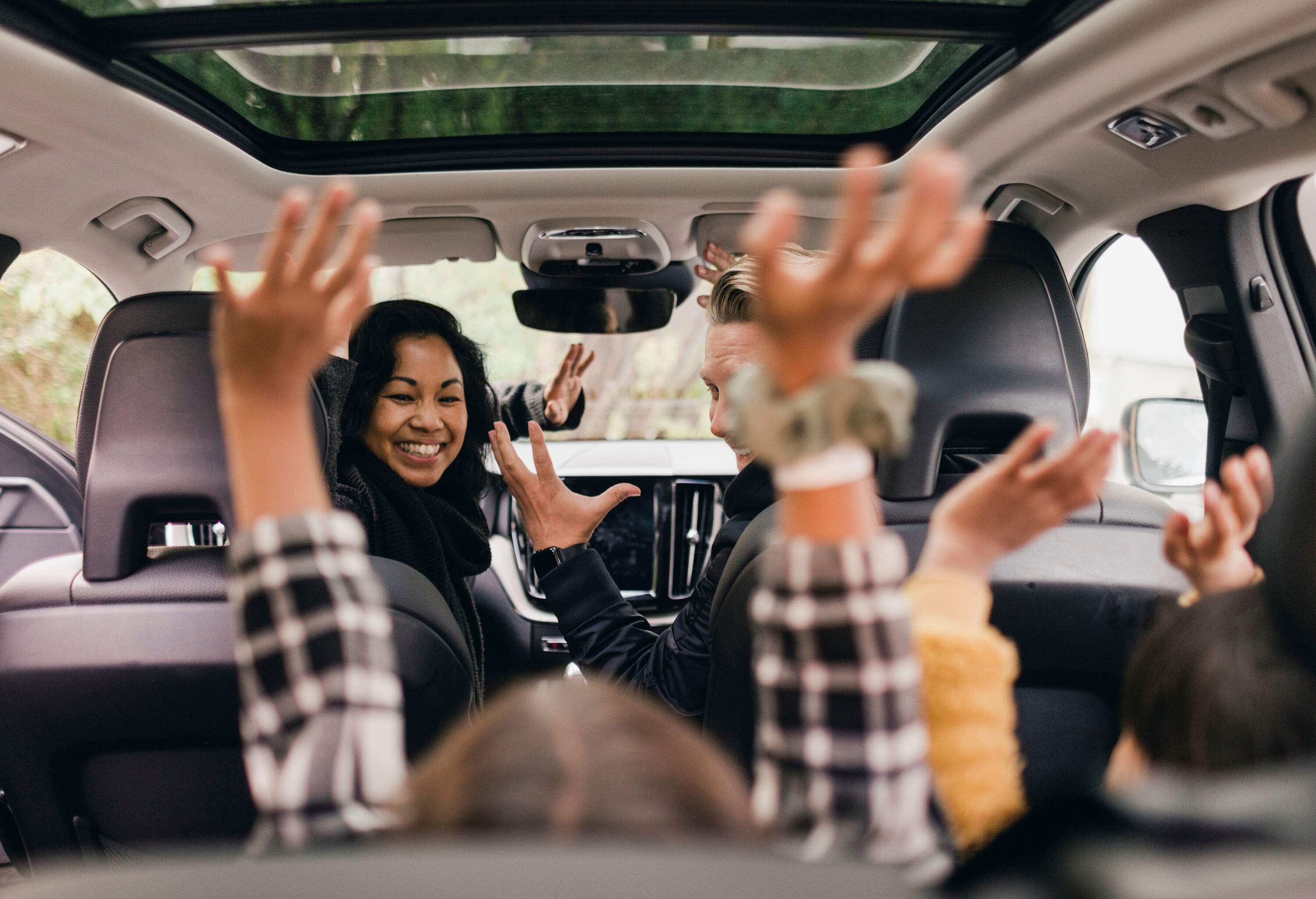 A family of four cheering in the car and excited to go on a road trip.