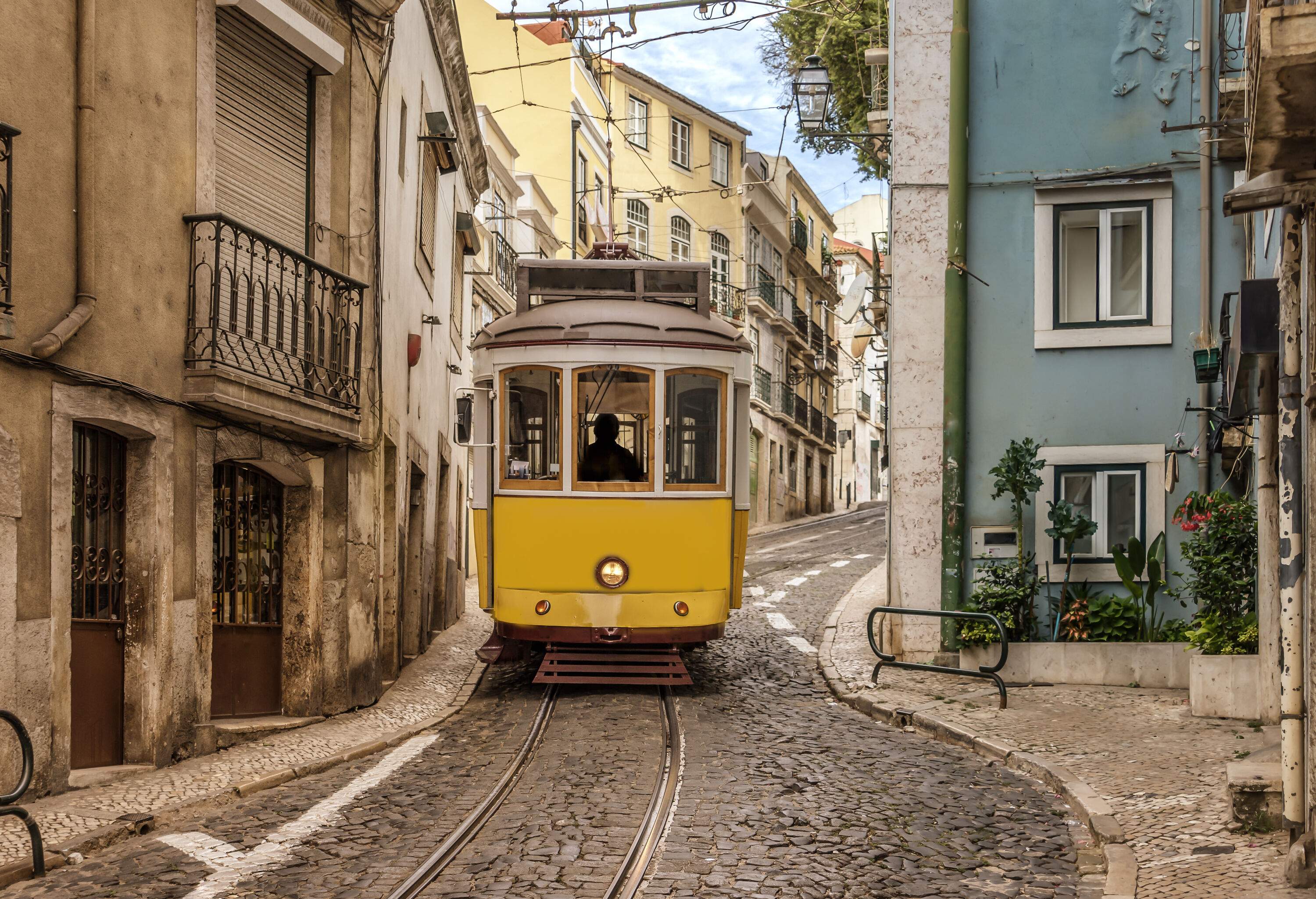 A vintage tram passing through a narrow lane surrounded by historic buildings.