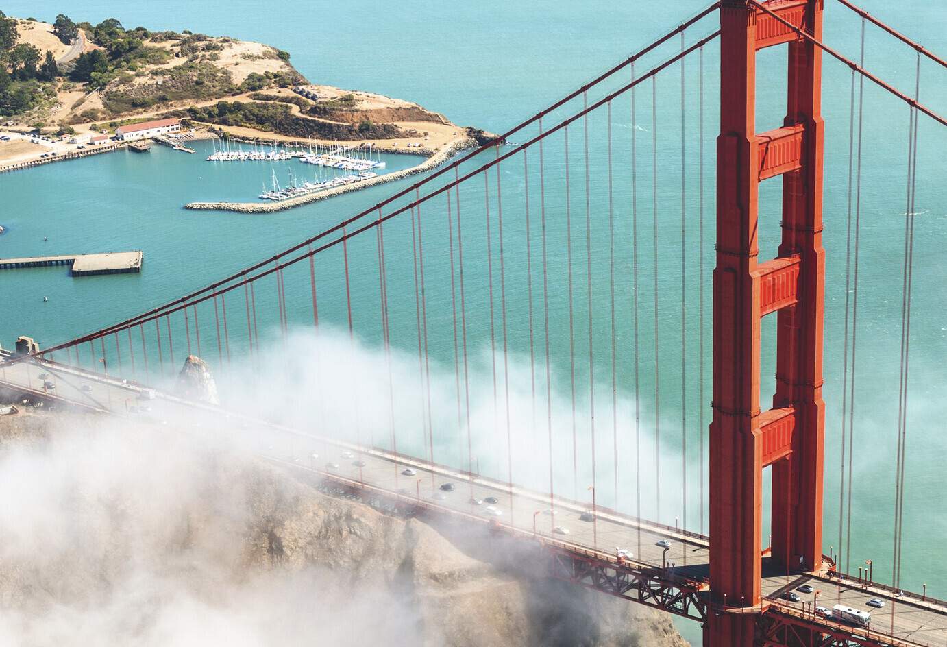 Aerial view of large metal red bridge over a bay surrounded by low clouds