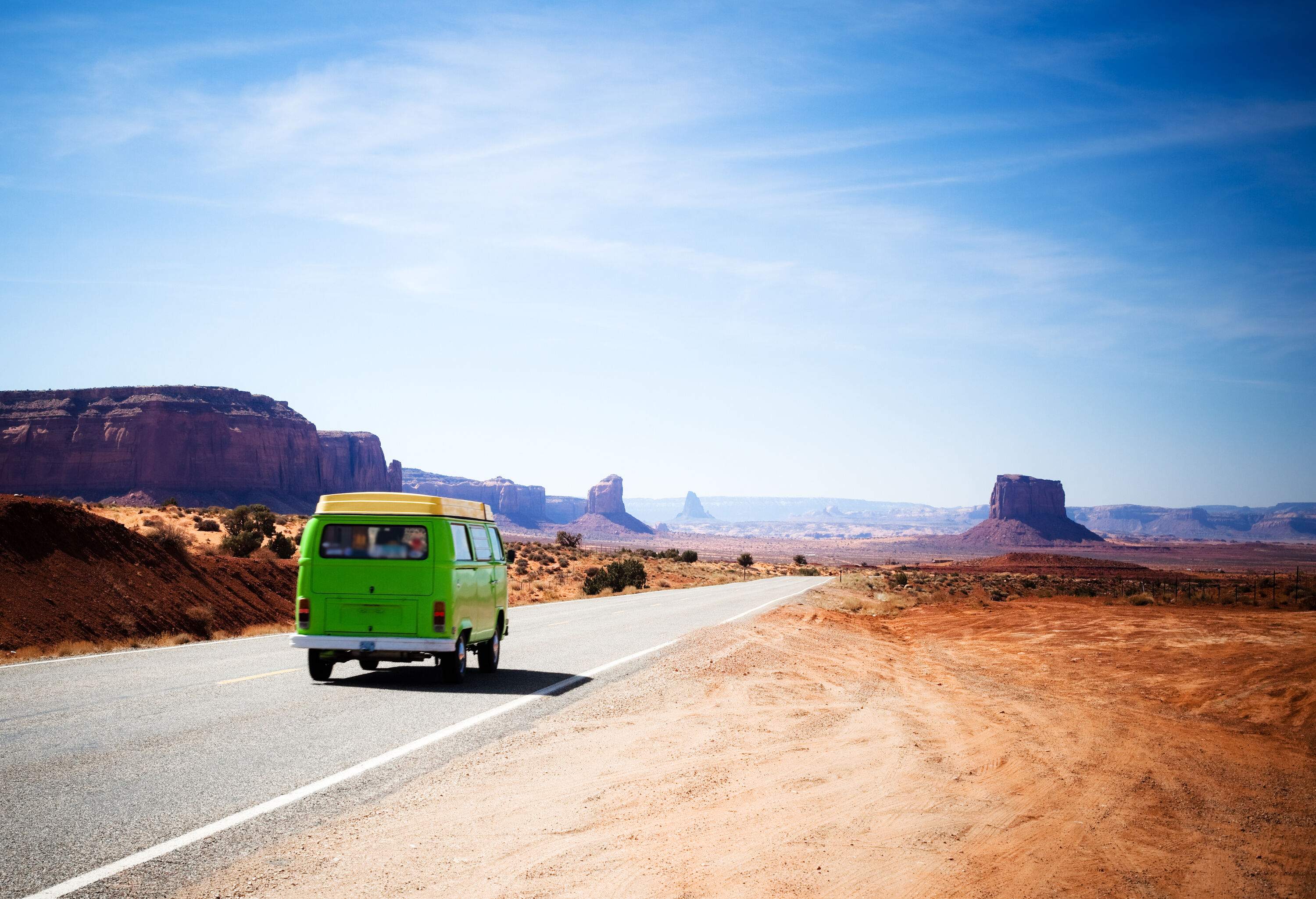 A bright green van driving down a roadway flanked by desolate landscape.