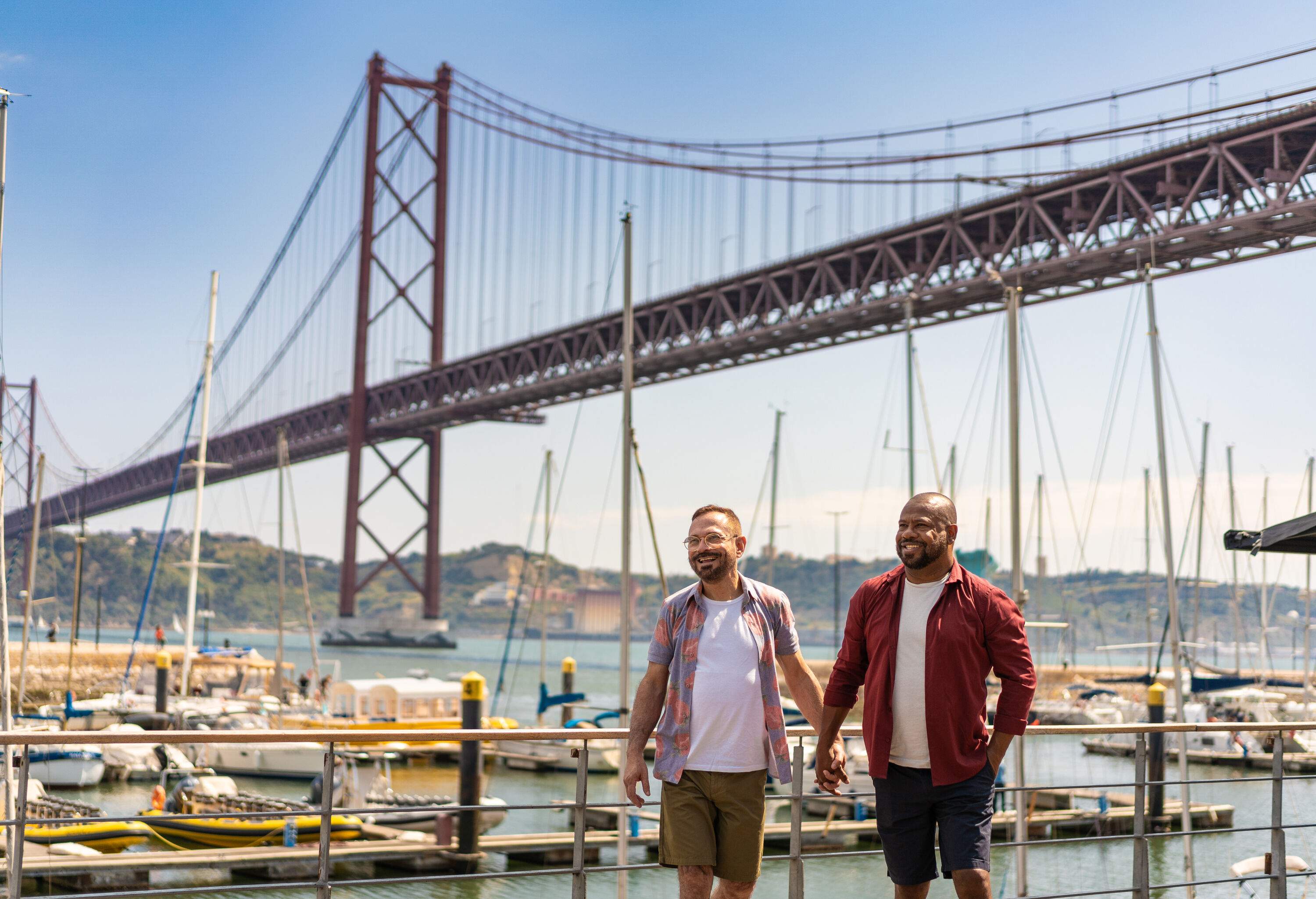 A happy gay couple walking hand in hand on the promenade against the busy harbour and an iconic bridge over the sea.