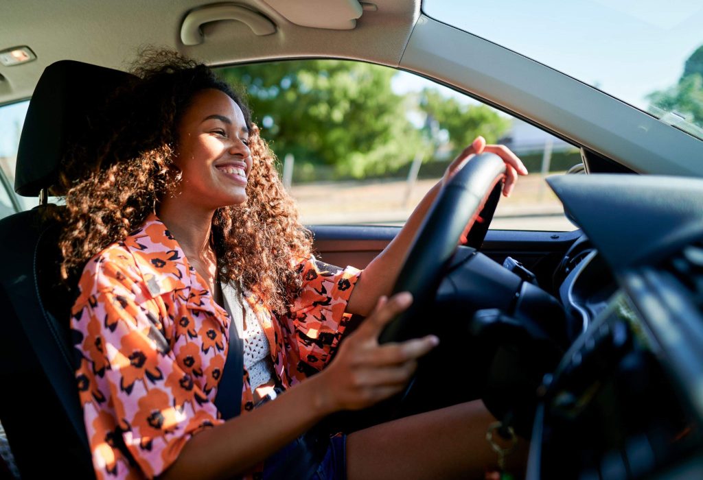 a smiling woman in a colorful outfit behind the wheel in a car 
