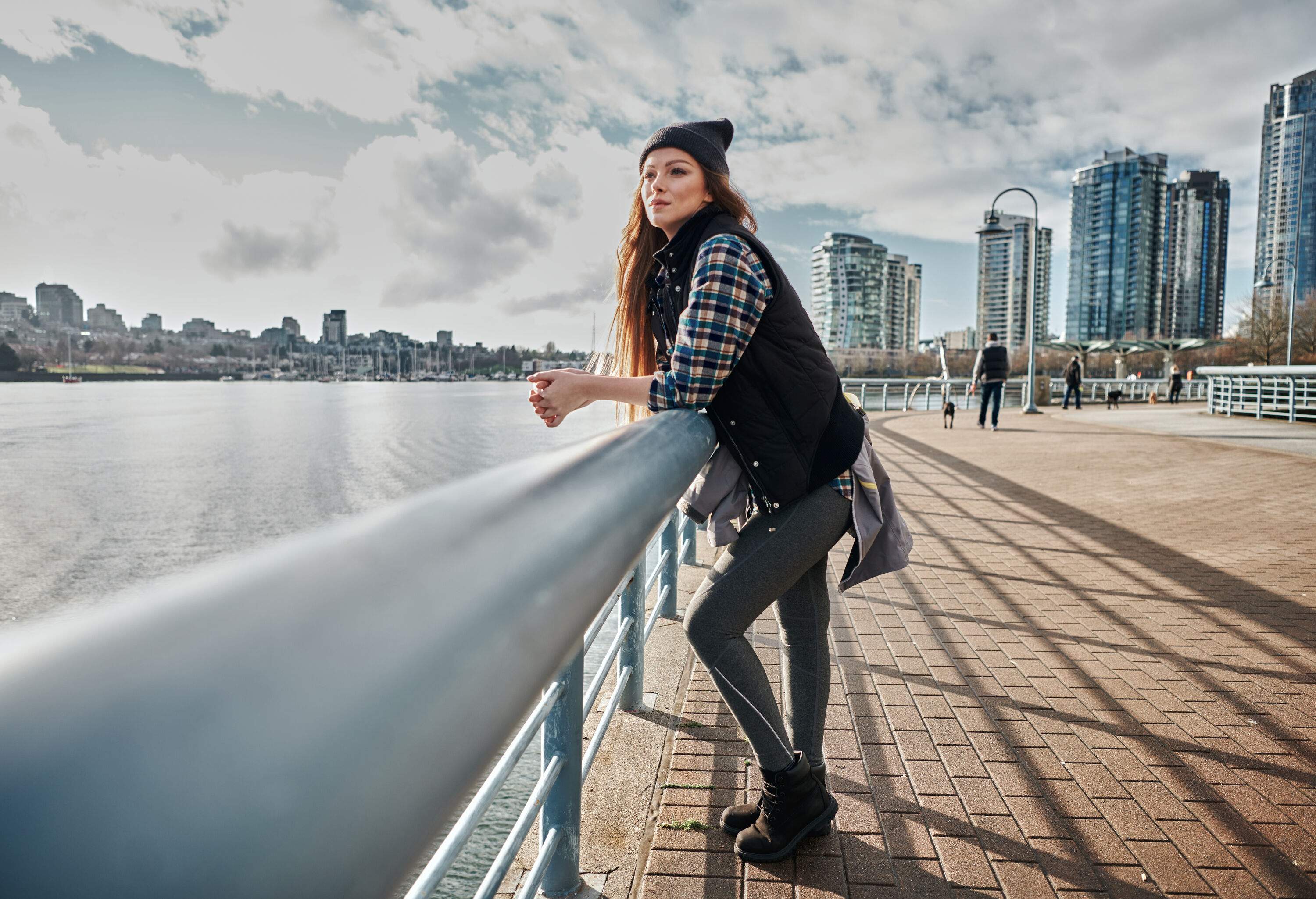A young woman, elbow resting on the guardrail, gazes pensively at the water while enjoying the serene atmosphere of the promenade.