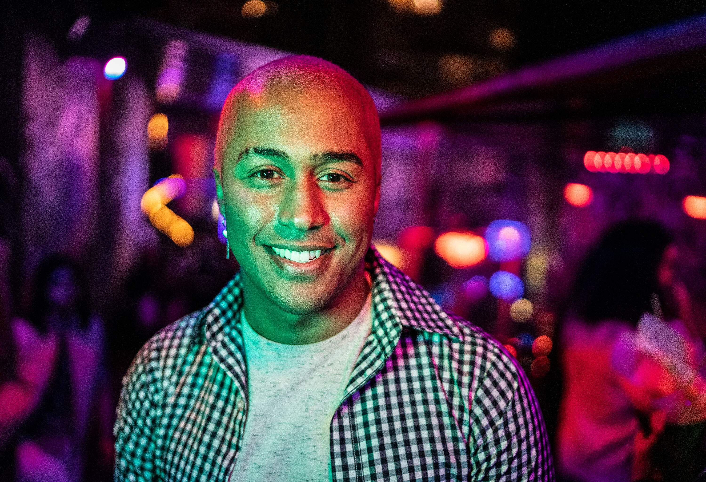 Portrait of a bald young man at a bright and colourful nightclub.