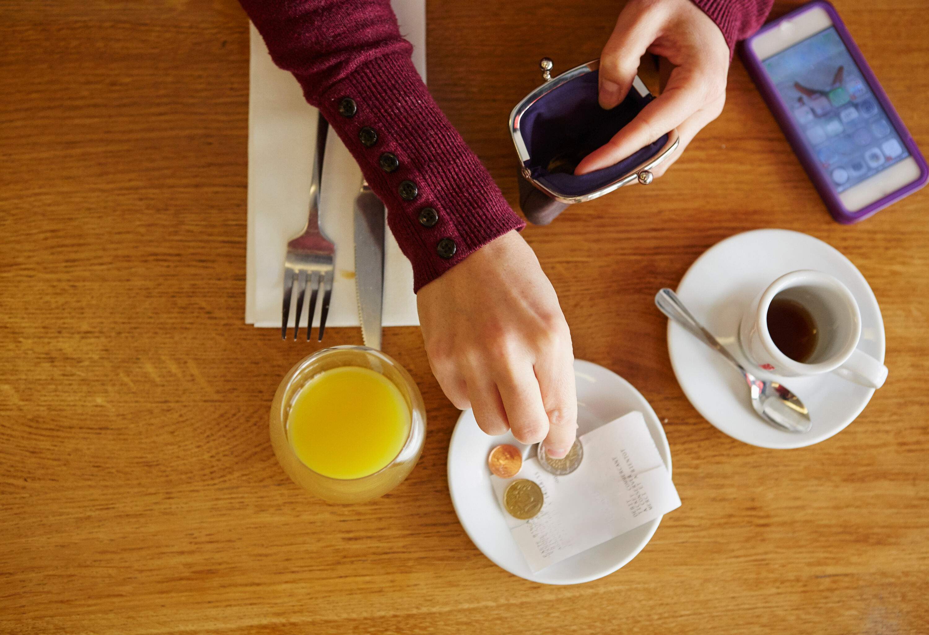 a topshot of a womans hands paying for her juice and a coffee on a table