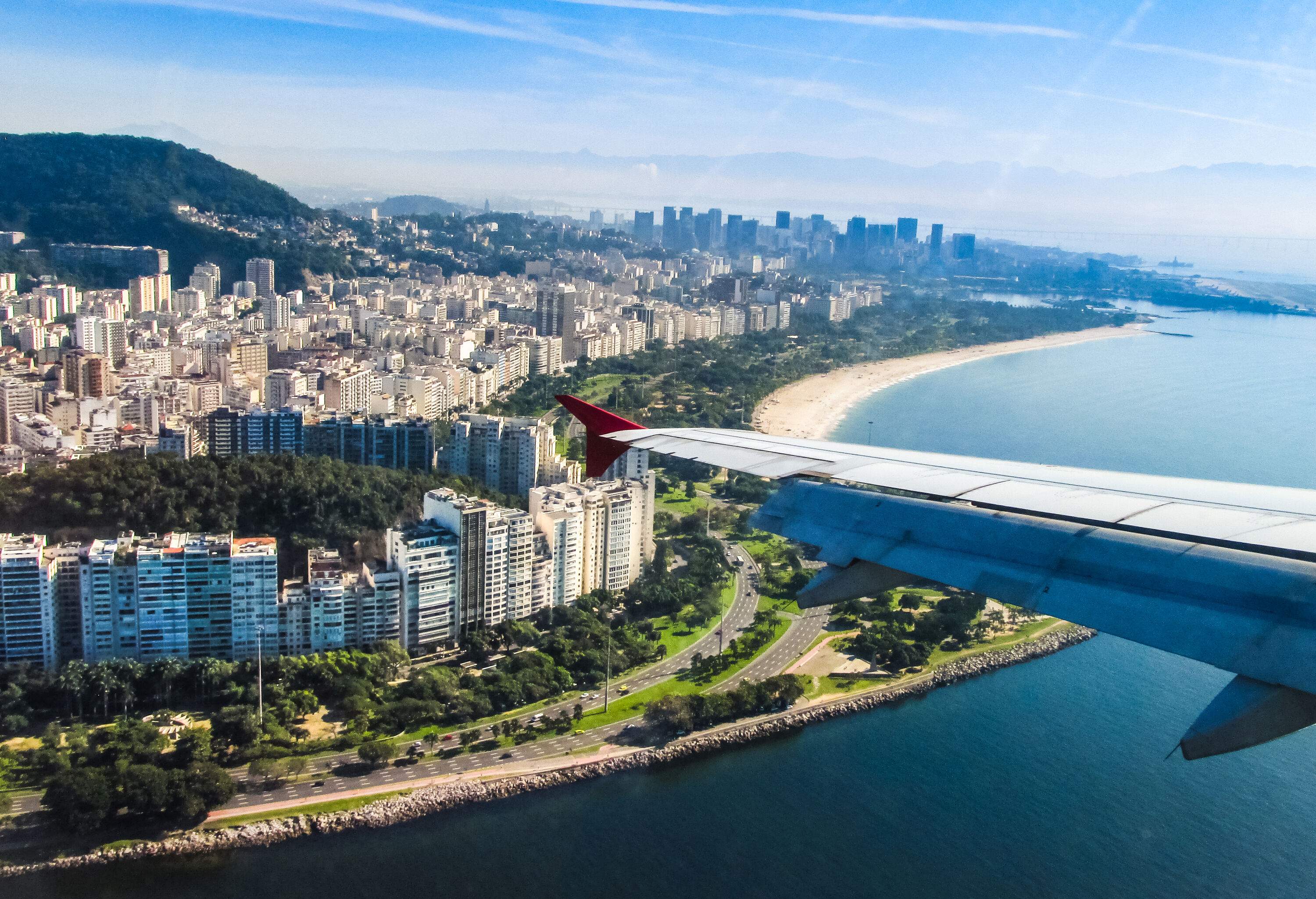 A coastal city with a cluster of high-rise buildings along a coastal road and beach as seen from an airplane.