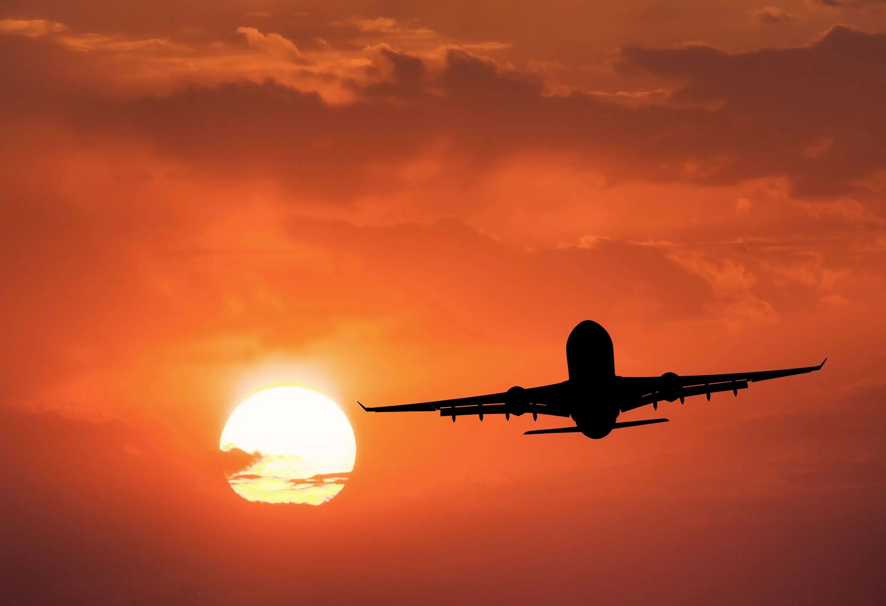 Silhouette of the aircraft and red sky with sun. Landscape with passenger airplane is flying in the sky with clouds at sunset. Travel background. Passenger airliner. Commercial airplane.