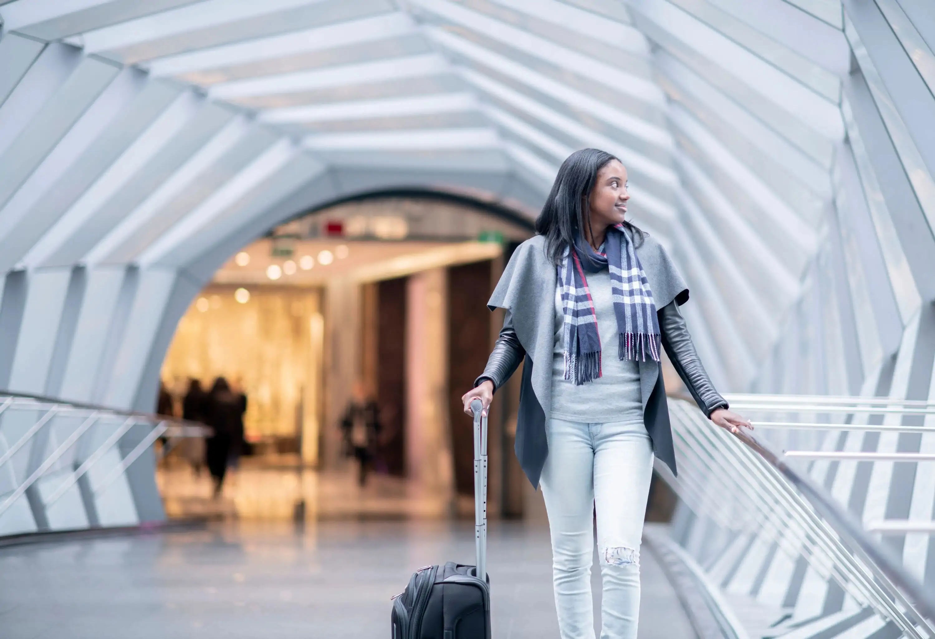 A woman of African descent is walking through an airport. She is carrying a suitcase and looking around.